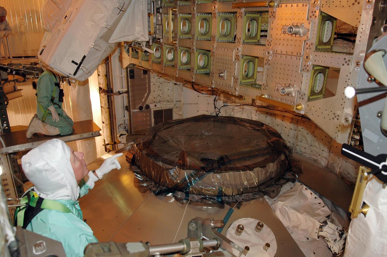 KENNEDY SPACE CENTER, FLA. - Seen in the foreground is STS-121 Michael Fossum, who is looking at the integrated cargo carrier, part of the payload for the mission, temporarily stored in the payload changeout room on Launch Pad 39B. He is dressed in a clean room suit, appropriate for the environmentally clean or "white room" condition in which the payload resides before being transferred to the shuttle's payload bay. In front of and below him is the multi-purpose logistics module Leonardo, which is carrying supplies and equipment for the International Space Station. The payload also includes the lightweight multi-purpose experiment support structure carrier. Crew members are at NASA's Kennedy Space Center for Terminal Countdown Demonstration Test activities, which include equipment familiarization and a simulated launch countdown. Mission STS-121 is scheduled for launch on Space Shuttle Discovery on July 1. Photo credit: NASA/Kim Shiflett