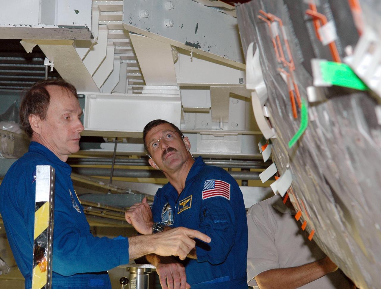 KENNEDY SPACE CENTER, FLA. -     In the Orbiter Processing Facility, STS-115 crew members examine tiles on the orbiter Atlantis,  the designated launch vehicle for their mission. From left are Mission Specialists Steven MacLean and Daniel Burbank.  MacLean represents the Canadian Space Agency.  The crew is at the center for Crew Equipment Interface Test activities, which involves equipment familiarization,  a routine part of astronaut training and launch preparations.  The mission will deliver the second port truss segment, the P3/P4 Truss, to attach to the first port truss segment, the P1 Truss, as well as deploy solar array set 2A and 4A.  Launch on Space Shuttle Atlantis is scheduled for late August.  Photo credit: NASA/Kim Shiflett