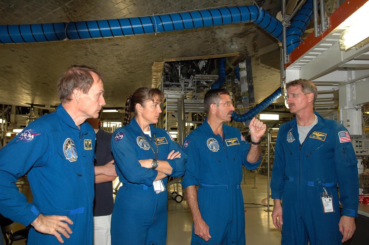 KENNEDY SPACE CENTER, FLA. -   In the Orbiter Processing Facility, STS-115 crew members discuss their examination of the orbiter Atlantis, seen above them.  From left are Mission Specialists Steven MacLean, who represents the Canadian Space Agency, Heidemarie Stefanyshyn-Piper, Daniel Burbank and Joseph Tanner.   The crew is at the center for Crew Equipment Interface Test activities, which involves equipment familiarization,  a routine part of astronaut training and launch preparations.  The mission will deliver the second port truss segment, the P3/P4 Truss, to attach to the first port truss segment, the P1 Truss, as well as deploy solar array set 2A and 4A.  Launch on Space Shuttle Atlantis is scheduled for late August.  Photo credit: NASA/Kim Shiflett