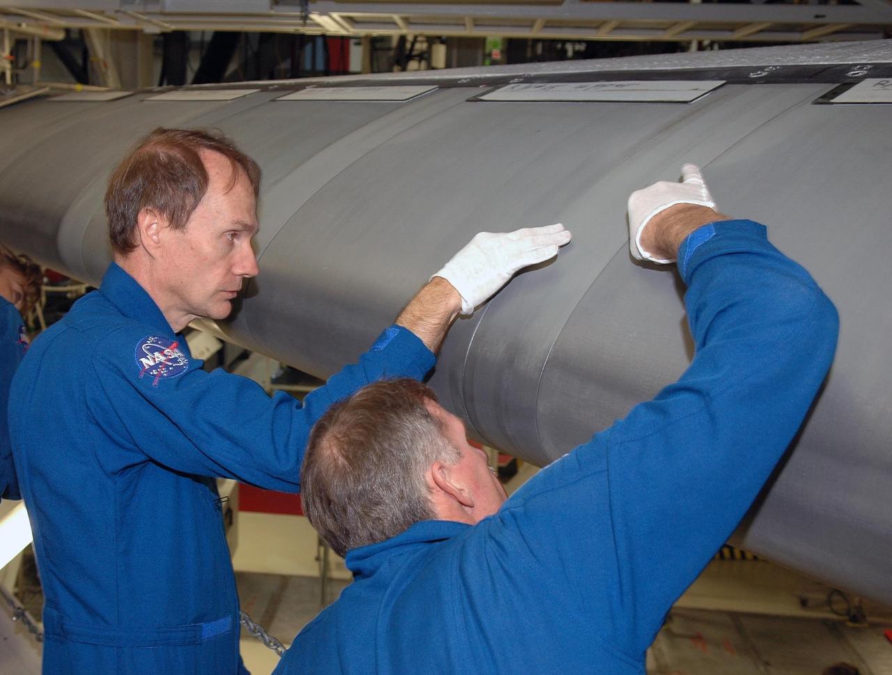 KENNEDY SPACE CENTER, FLA. - In the Orbiter Processing Facility, STS-115 crew members examine the edge of the wing on the orbiter Atlantis, the designated launch vehicle for their mission. From left are Mission Specialists Steven MacLean, who represents the Canadian Space Agency, and Joseph Tanner.  The crew is at the center for Crew Equipment Interface Test activities, which involves equipment familiarization,  a routine part of astronaut training and launch preparations.  The mission will deliver the second port truss segment, the P3/P4 Truss, to attach to the first port truss segment, the P1 Truss, as well as deploy solar array set 2A and 4A.  Launch on Space Shuttle Atlantis is scheduled for late August.  Photo credit: NASA/Kim Shiflett