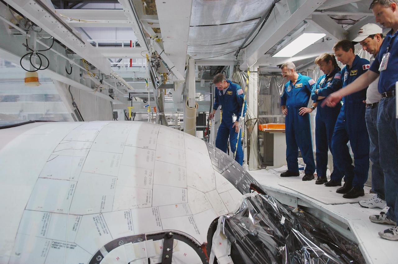 KENNEDY SPACE CENTER, FLA. - In the Orbiter Processing Facility, STS-115 Mission Specialist Joseph Tanner takes a closer look at the orbiter Atlantis, the designated launch vehicle for the mission..  Looking on (from left) are Mission Specialists Daniel Burbank, Heidemarie Stefanyshyn-Piper and Steven MacLean, who represents the Canadian Space Agency.  The crew is at the center for Crew Equipment Interface Test activities, which involves equipment familiarization,  a routine part of astronaut training and launch preparations.  The mission will deliver the second port truss segment, the P3/P4 Truss, to attach to the first port truss segment, the P1 Truss, as well as deploy solar array set 2A and 4A.  Launch on Space Shuttle Atlantis is scheduled for late August.  Photo credit: NASA/Kim Shiflett