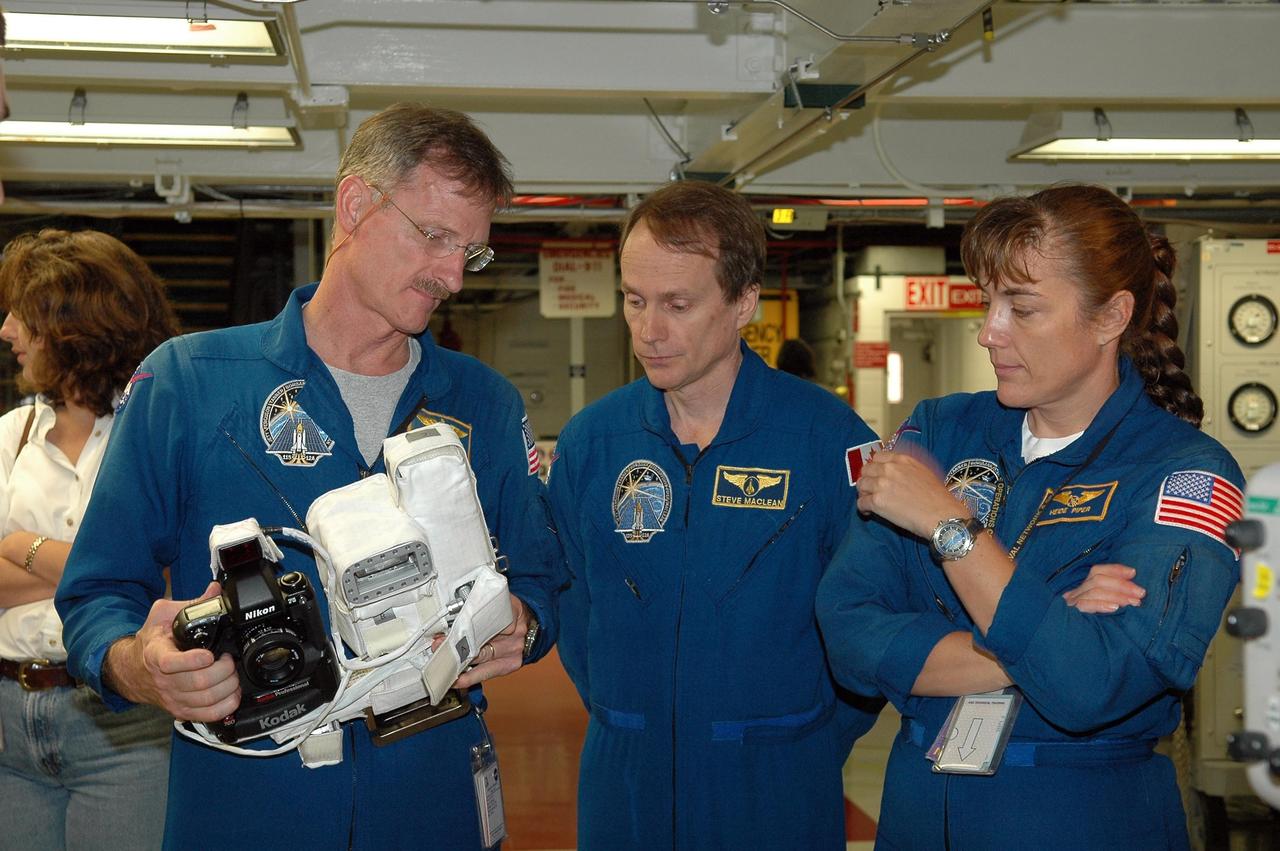 KENNEDY SPACE CENTER, FLA. - In the Orbiter Processing Facility, STS-115 Mission Specialist Joseph Tanner gets familiar with a camera that is a mockup of one the crew will use to take photographs on-orbit.  With him are Mission Specialists Steven MacLean, who represents the Canadian Space Agency, and Heidemarie Stefanyshyn-Piper.  The crew is at the center for Crew Equipment Interface Test activities, which involves equipment familiarization,  a routine part of astronaut training and launch preparations.  The mission will deliver the second port truss segment, the P3/P4 Truss, to attach to the first port truss segment, the P1 Truss, as well as deploy solar array set 2A and 4A.  Launch on Space Shuttle Atlantis is scheduled for late August.  Photo credit: NASA/Kim Shiflett