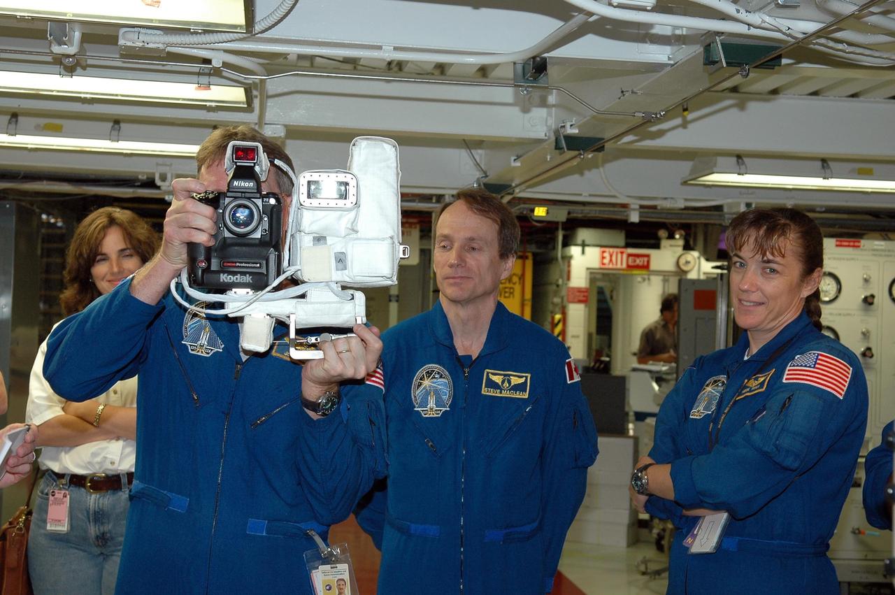 KENNEDY SPACE CENTER, FLA. - In the Orbiter Processing Facility, STS-115 Mission Specialist Joseph Tanner practices using a camera that is a mockup of one the crew will use to take photographs on-orbit.  With him are Mission Specialists Steven MacLean, who represents the Canadian Space Agency, and Heidemarie Stefanyshyn-Piper.  The crew is at the center for Crew Equipment Interface Test activities, which involves equipment familiarization,  a routine part of astronaut training and launch preparations.  The mission will deliver the second port truss segment, the P3/P4 Truss, to attach to the first port truss segment, the P1 Truss, as well as deploy solar array set 2A and 4A.  Launch on Space Shuttle Atlantis is scheduled for late August.  Photo credit: NASA/Kim Shiflett