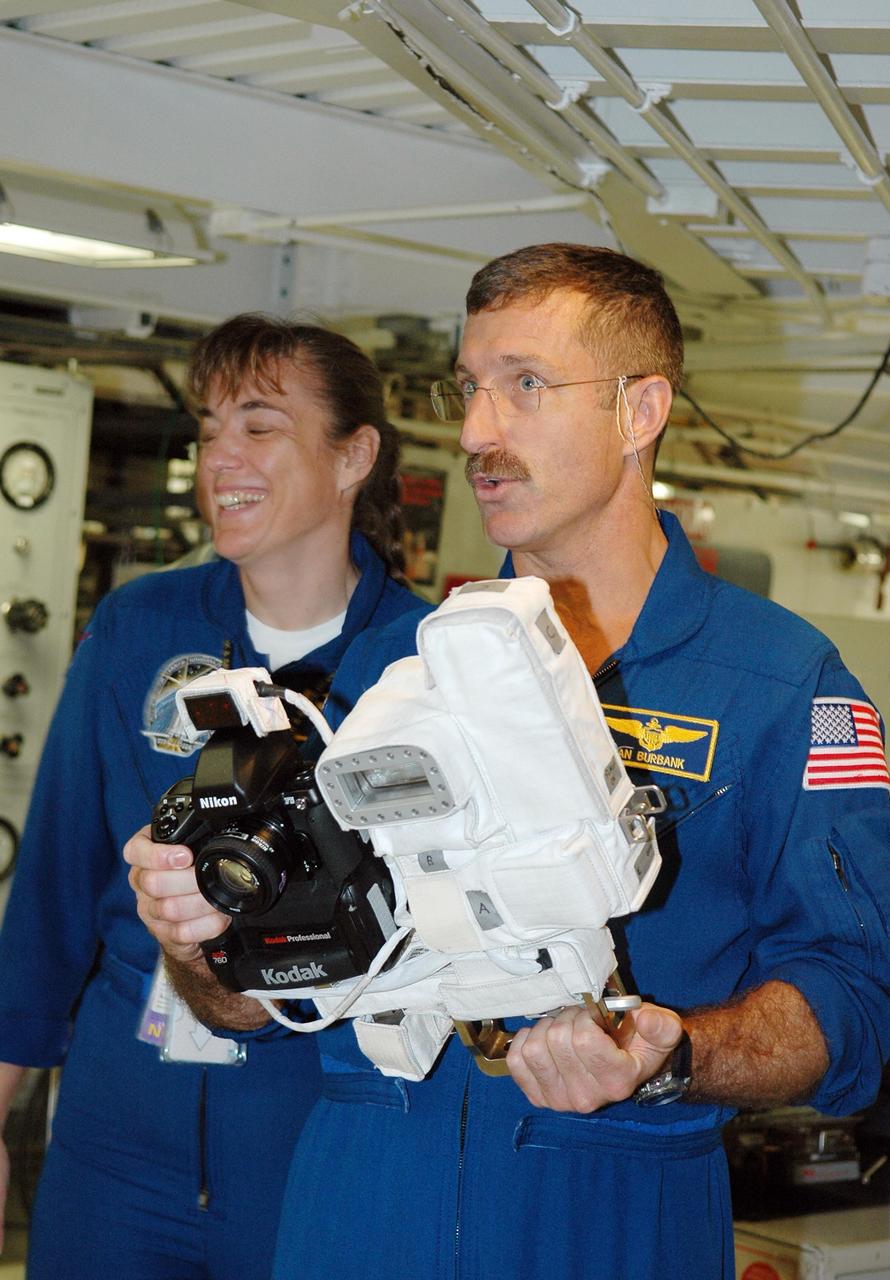 KENNEDY SPACE CENTER, FLA. - In the Orbiter Processing Facility, STS-115 Mission Specialist Daniel Burbank holds a camera that is a mockup of one the crew will use to take photographs on-orbit. At left is Mission Specialist Heidemarie Stefanyshyn-Piper.  The crew is at the center for Crew Equipment Interface Test activities, which involves equipment familiarization,  a routine part of astronaut training and launch preparations.  The mission will deliver the second port truss segment, the P3/P4 Truss, to attach to the first port truss segment, the P1 Truss, as well as deploy solar array set 2A and 4A.  Launch on Space Shuttle Atlantis is scheduled for late August.  Photo credit: NASA/Kim Shiflett