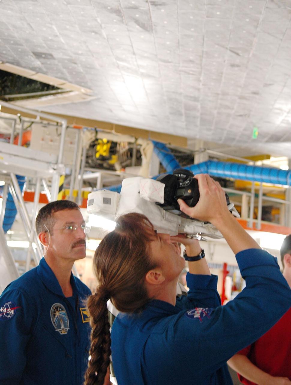 KENNEDY SPACE CENTER, FLA. - In the Orbiter Processing Facility, STS-115 Mission Specialist Heidemarie Stefanyshyn-Piper practices using a camera that is a mockup of one the crew will use to take photographs on-orbit. At left is Mission Specialist Daniel Burbank.  The crew is at the center for Crew Equipment Interface Test activities, which involves equipment familiarization,  a routine part of astronaut training and launch preparations.  The mission will deliver the second port truss segment, the P3/P4 Truss, to attach to the first port truss segment, the P1 Truss, as well as deploy solar array set 2A and 4A.  Launch on Space Shuttle Atlantis is scheduled for late August.  Photo credit: NASA/Kim Shiflett