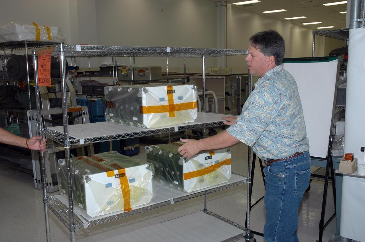 KENNEDY SPACE CENTER, FLA. -   In the Space Station Processing Facility at NASA's Kennedy Space Center,  John Hoog reaches for a container filled with prepared meals for the crew of mission STS-121 to secure it for flight.  Hoog is a USA-FCE/EVA representative from Johnson Space Center.  Astronauts select their own menus from a large array of food items. Astronauts are supplied with three balanced meals, plus snacks.  Foods flown on space missions are researched and developed at the Space Food Systems Laboratory at the Johnson Space Center (JSC) in Houston, which is staffed by food scientists, dietitians and engineers. Foods are analyzed through nutritional analysis, sensory evaluation, storage studies, packaging evaluations and many other methods.   Each astronaut’s food is stored aboard the space shuttle and is identified by a colored dot affixed to each package.  Launch of Space Shuttle Discovery on mission STS-121 is scheduled for July 1.  Photo credit: NASA/Jack Pfaller