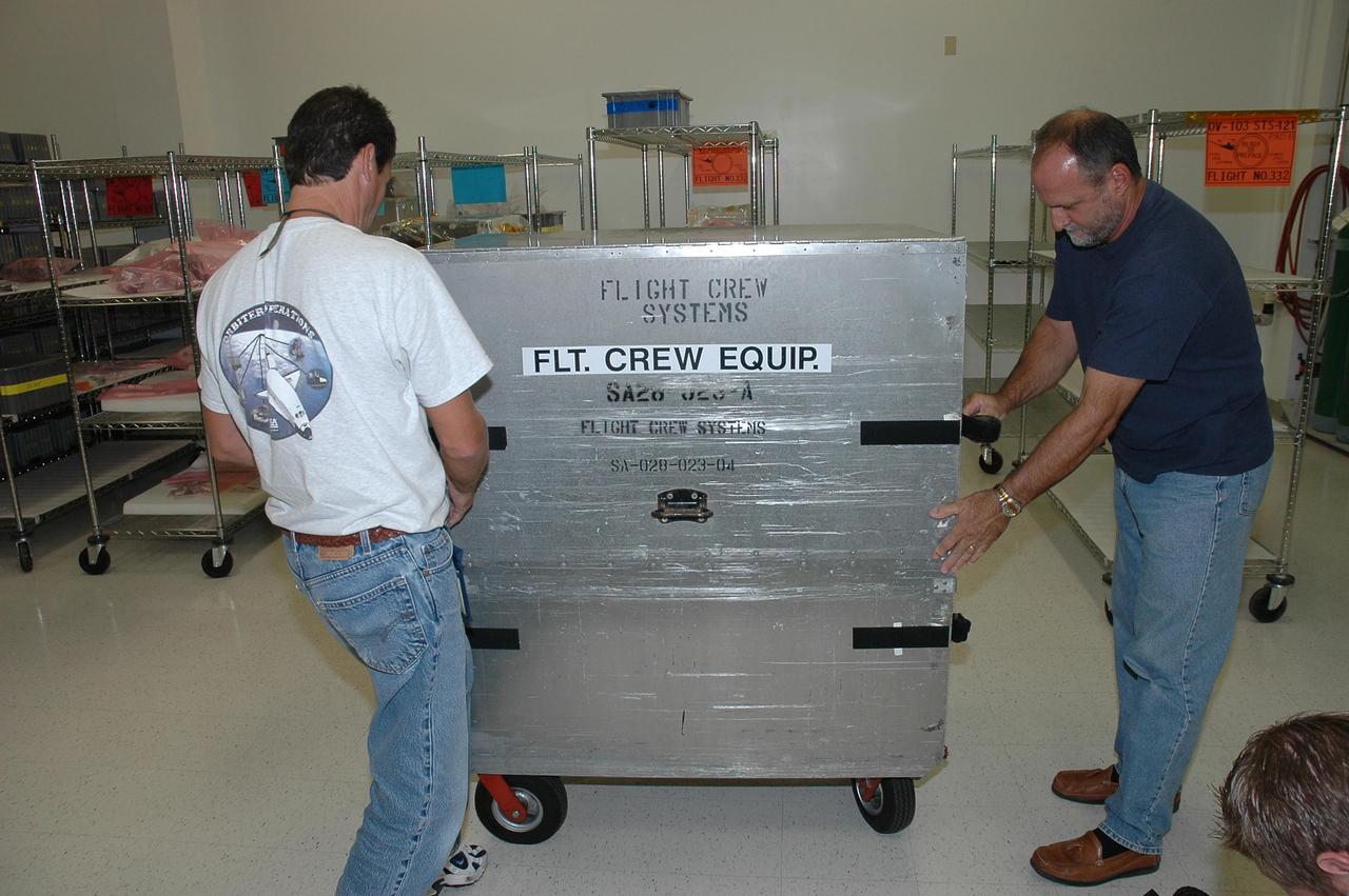 KENNEDY SPACE CENTER, FLA. -    In the Space Station Processing Facility at NASA's Kennedy Space Center, flight crew systems technician Troy Mann and flight crew systems manager Jim Blake secure the storage boxes holding the food containers that will be stowed on Space Shuttle Discovery for the flight of mission STS-121.  The containers hold meals prepared for the mission crew.   Astronauts select their own menus from a large array of food items. Astronauts are supplied with three balanced meals, plus snacks.  Foods flown on space missions are researched and developed at the Space Food Systems Laboratory at the Johnson Space Center (JSC) in Houston, which is staffed by food scientists, dietitians and engineers. Foods are analyzed through nutritional analysis, sensory evaluation, storage studies, packaging evaluations and many other methods.   Each astronaut’s food is stored aboard the space shuttle and is identified by a colored dot affixed to each package.  Launch of Space Shuttle Discovery on mission STS-121 is scheduled for July 1.  Photo credit: NASA/Jack Pfaller