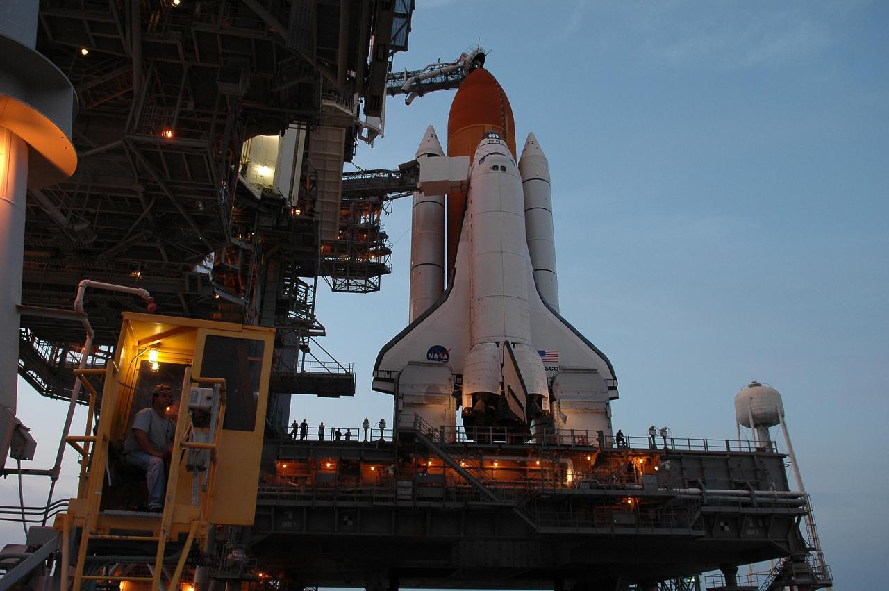 KENNEDY SPACE CENTER, FLA. -  Lights glow around Space Shuttle Discovery as it stands revealed after rollback of the rotating service structure in preparation for launch July 1 on mission STS-121.  Above the golden external tank is the vent hood (known as the "beanie cap") at the end of the gaseous oxygen vent arm. Vapors are created as the liquid oxygen in the external tank boil off. The hood vents the gaseous oxygen vapors away from the space shuttle vehicle.  The RSS provides protected access to the orbiter for changeout and servicing of payloads at the pad. The structure is supported by a rotating bridge that pivots about a vertical axis on the west side of the pad's flame trench. The hinge column rests on the pad surface and is braced to the fixed service structure. Support for the outer end of the bridge is provided by two eight-wheel, motor-driven trucks that move along circular twin rails installed flush with the pad surface. The track crosses the flame trench on a permanent bridge.  The RSS is 102 feet long, 50 feet wide and 130 feet high. The structure has orbiter access platforms at five levels to provide access to the payload bay while the orbiter is being serviced in the RSS. Each platform has independent extendable planks that can be arranged to conform to a payload's configuration.  This mission is the 115th shuttle flight and the 18th U.S. flight to the International Space Station. Photo credit: NASA/Kim Shiflett