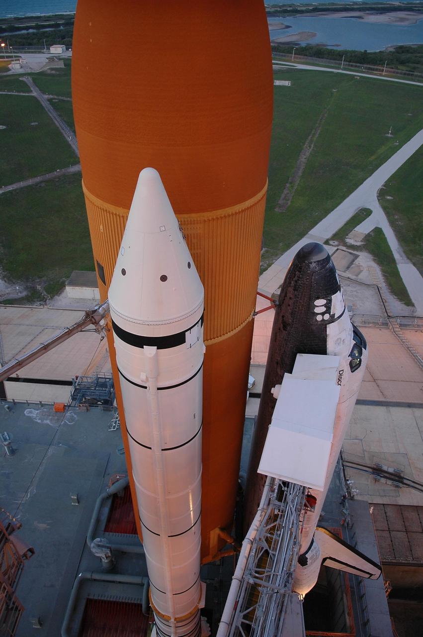 KENNEDY SPACE CENTER, FLA. -   Viewed from an upper level of the fixed service structure on Launch Pad 39B, Space Shuttle Discovery looms over the pad and surrounding area after rollback of the rotating service structure (RSS).  The rollback was in preparation for launch July 1 on mission STS-121.  Extending toward the cockpit of the shuttle is the orbiter access arm with the White Room extended.  The White Room provides access into the orbiter for the astronauts.  The RSS provides protected access to the orbiter for changeout and servicing of payloads at the pad. The structure is supported by a rotating bridge that pivots about a vertical axis on the west side of the pad's flame trench. The hinge column rests on the pad surface and is braced to the fixed service structure. Support for the outer end of the bridge is provided by two eight-wheel, motor-driven trucks that move along circular twin rails installed flush with the pad surface. The track crosses the flame trench on a permanent bridge.  The RSS is 102 feet long, 50 feet wide and 130 feet high. The structure has orbiter access platforms at five levels to provide access to the payload bay while the orbiter is being serviced in the RSS. Each platform has independent extendable planks that can be arranged to conform to a payload's configuration.  This mission is the 115th shuttle flight and the 18th U.S. flight to the International Space Station. Photo credit: NASA/Kim Shiflett