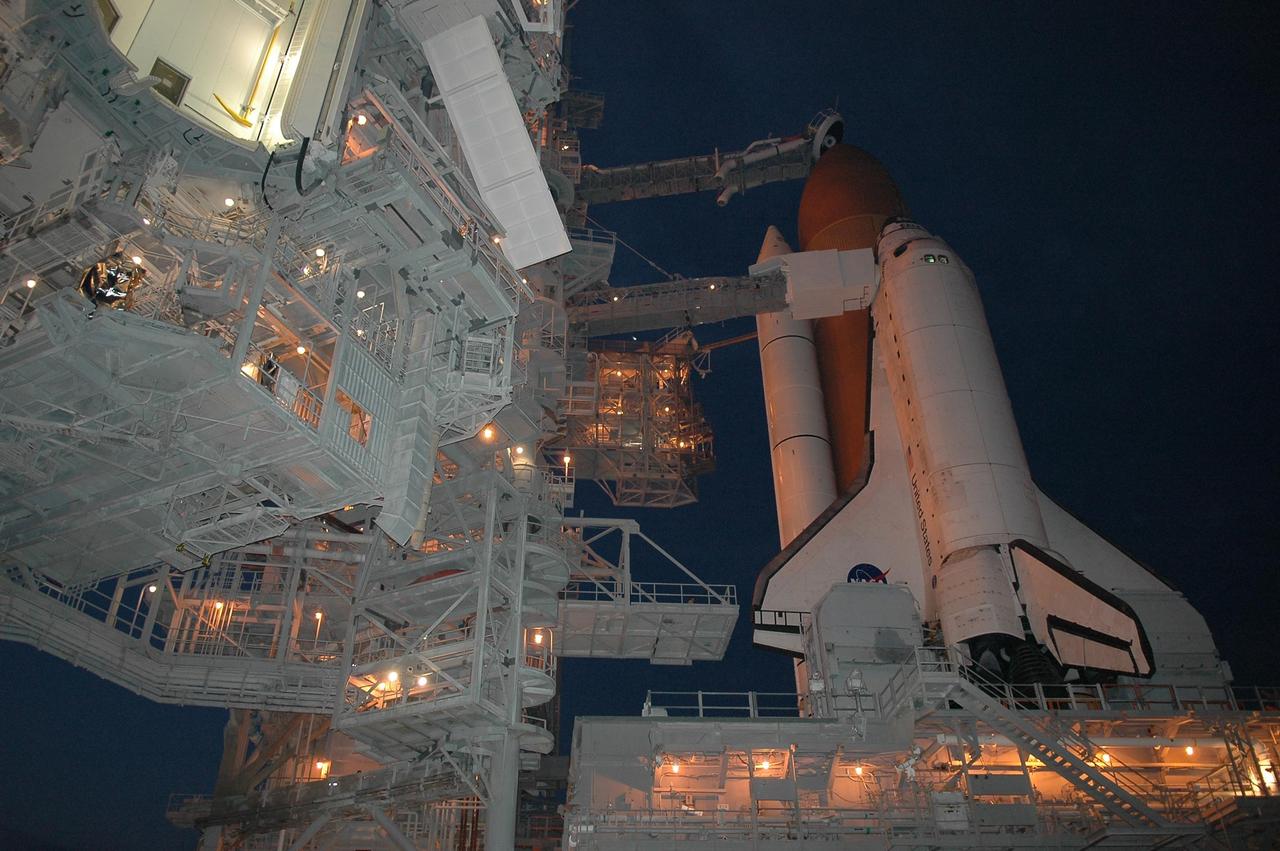 KENNEDY SPACE CENTER, FLA. -   After rollback of the rotating service structure (RSS) on Launch Pad 39B, Space Shuttle Discovery stands bathed in lights from the RSS and fixed service structure.  The rollback was in preparation for launch July 1 on mission STS-121.  Extending toward the cockpit of the shuttle is the orbiter access arm with the White Room extended.  The White Room provides access into the orbiter for the astronauts.  The RSS provides protected access to the orbiter for changeout and servicing of payloads at the pad. The structure is supported by a rotating bridge that pivots about a vertical axis on the west side of the pad's flame trench. The hinge column rests on the pad surface and is braced to the fixed service structure. Support for the outer end of the bridge is provided by two eight-wheel, motor-driven trucks that move along circular twin rails installed flush with the pad surface. The track crosses the flame trench on a permanent bridge.  The RSS is 102 feet long, 50 feet wide and 130 feet high. The structure has orbiter access platforms at five levels to provide access to the payload bay while the orbiter is being serviced in the RSS. Each platform has independent extendable planks that can be arranged to conform to a payload's configuration.  This mission is the 115th shuttle flight and the 18th U.S. flight to the International Space Station. Photo credit: NASA/Kim Shiflett