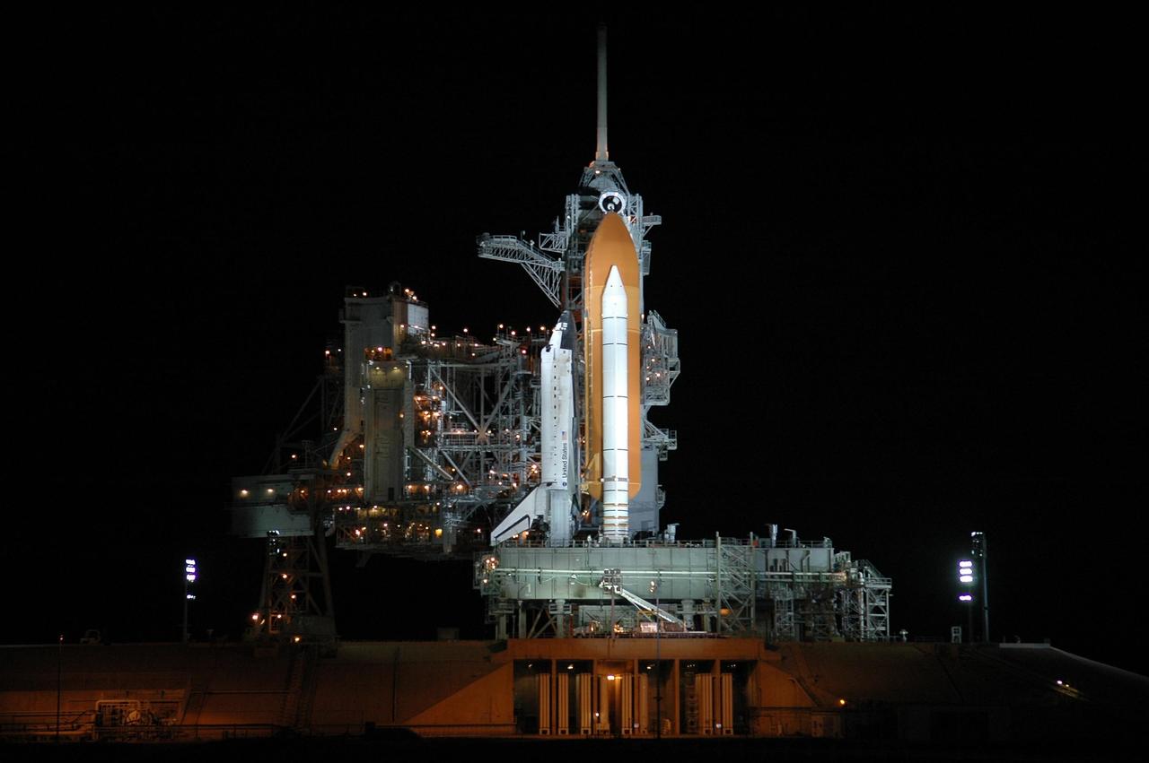 KENNEDY SPACE CENTER, FLA. -   After rollback of the rotating service structure (RSS) on Launch Pad 39B, Space Shuttle Discovery stands bathed in spotlights.  Beneath the shuttle is the mobile launcher platform, which spans the flame trench below.  The flame deflector system includes an inverted, V-shaped steel structure that receives and deflects the flames from the orbiter main engines on one side; the opposite side deflects the flames from the solid rocket boosters.  The RSS provides protected access to the orbiter for changeout and servicing of payloads at the pad. The structure is supported by a rotating bridge that pivots about a vertical axis on the west side of the pad's flame trench. The hinge column rests on the pad surface and is braced to the fixed service structure. Support for the outer end of the bridge is provided by two eight-wheel, motor-driven trucks that move along circular twin rails installed flush with the pad surface. The track crosses the flame trench on a permanent bridge.  The RSS is 102 feet long, 50 feet wide and 130 feet high. The structure has orbiter access platforms at five levels to provide access to the payload bay while the orbiter is being serviced in the RSS. Each platform has independent extendable planks that can be arranged to conform to a payload's configuration.  This mission is the 115th shuttle flight and the 18th U.S. flight to the International Space Station. Photo credit: NASA/Kim Shiflett