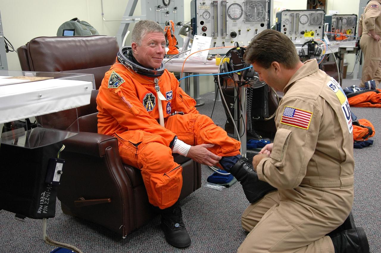 KENNEDY SPACE CENTER, FLA. -    STS-121 Mission Specialist Michael Fossum is helped with his boot during suitup for launch today on Space Shuttle Discovery. The launch is the 115th shuttle flight and the 18th U.S. flight to the International Space Station.  During the 12-day mission, the STS-121 crew will test new equipment and procedures to improve shuttle safety, as well as deliver supplies and make repairs to the International Space Station.  Photo credit: NASA/Kim Shiflett