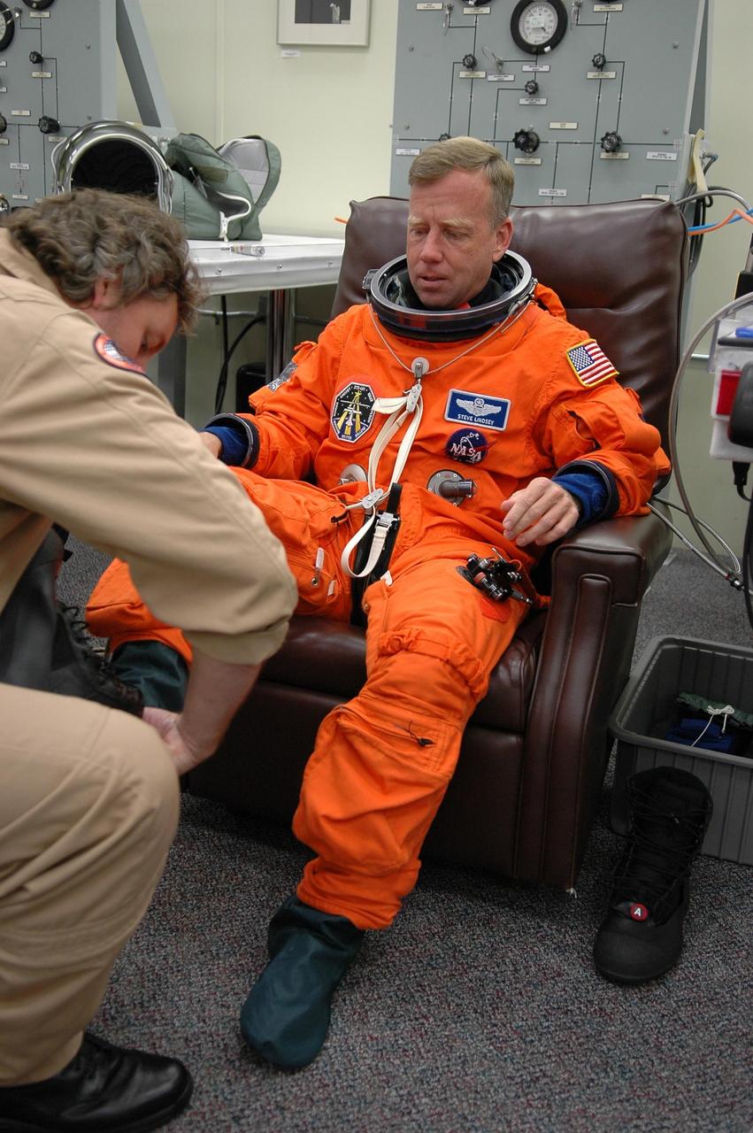 KENNEDY SPACE CENTER, FLA. -   STS-121 Commander Steven Lindsey is helped with his boot during suitup before heading to Launch Pad 39B and the third attempt at liftoff on mission STS-121. The launch of Space Shuttle Discovery on mission STS-121 is the 115th shuttle flight and the 18th U.S. flight to the International Space Station.  During the 12-day mission, the STS-121 crew will test new equipment and procedures to improve shuttle safety, as well as deliver supplies and make repairs to the International Space Station.  Photo credit: NASA/Kim Shiflett