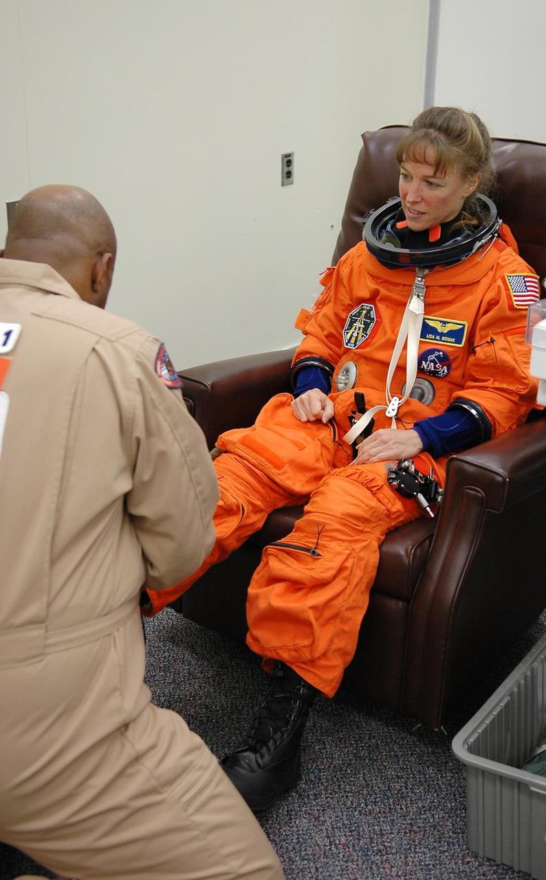 KENNEDY SPACE CENTER, FLA. - STS-121 Mission Specialist Lisa Nowak is helped with her boots during suitup before heading to Launch Pad 39B and a third launch attempt. The July 2 launch attempt was scrubbed due to the presence of showers and thunderstorms within the surrounding area of the launch site. The launch of Space Shuttle Discovery on mission STS-121 is the 115th shuttle flight and the 18th U.S. flight to the International Space Station. During the 12-day mission, the STS-121 crew will test new equipment and procedures to improve shuttle safety, as well as deliver supplies and make repairs to the International Space Station. Photo credit: NASA/Kim Shiflett