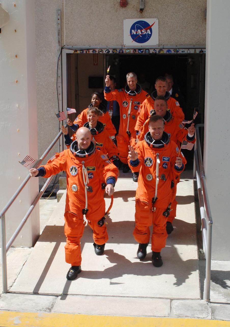 KENNEDY SPACE CENTER, FLA. - The STS-121 crew displays the spirit of the Fourth of July holiday with their flags and their eagerness to launch as they stride out of the Operations and Checkout Building. Leading the way are Pilot Mark Kelly (left) and Commander Steven Lindsey (right). Behind them are Mission Specialists (second row) Lisa Nowak and Michael Fossum; (third row) Stephanie Wilson and Piers Sellers; and (at the rear) Thomas Reiter, who represents the European Space Agency. The July 2 launch attempt was scrubbed due to the presence of showers and thunderstorms within the surrounding area of the launch site. The launch of Space Shuttle Discovery on mission STS-121 is the 115th shuttle flight and the 18th U.S. flight to the International Space Station. During the 12-day mission, the STS-121 crew will test new equipment and procedures to improve shuttle safety, as well as deliver supplies and make repairs to the International Space Station. Photo credit: NASA/Kim Shiflett