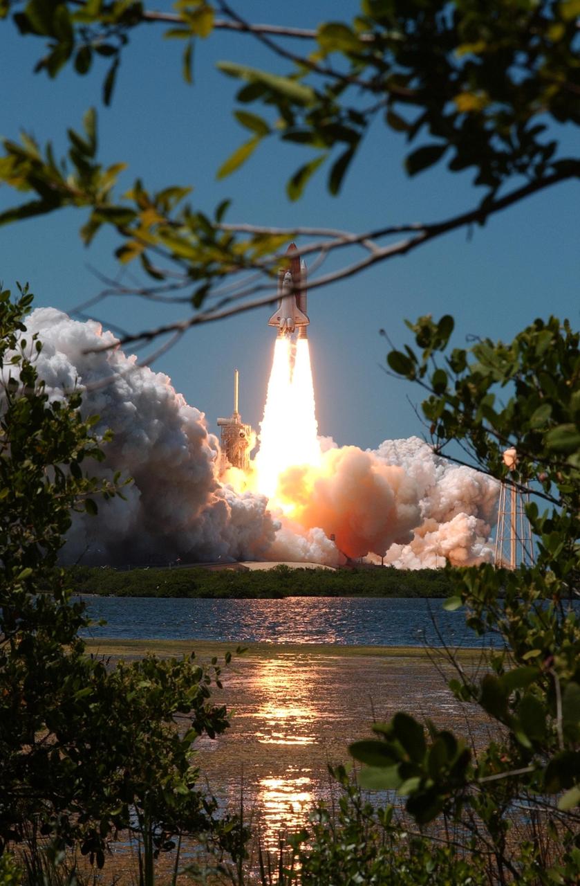 KENNEDY SPACE CENTER, FLA. - Framed by the woods across the pond, Space Shuttle Discovery kicks off the Fourth of July fireworks with its own fiery display as it rockets into the blue sky, spewing foam and smoke over the ground, on mission STS-121. It was the third launch attempt in four days; the others were scrubbed due to weather concerns. Liftoff was on-time at 2:38 p.m. EDT. During the 12-day mission, the STS-121 crew of seven will test new equipment and procedures to improve shuttle safety, as well as deliver supplies and make repairs to the International Space Station. Landing is scheduled for July 16 or 17 at Kennedy's Shuttle Landing Facility. Photo credit: NASA/Sandy Joseph, Robert Murray