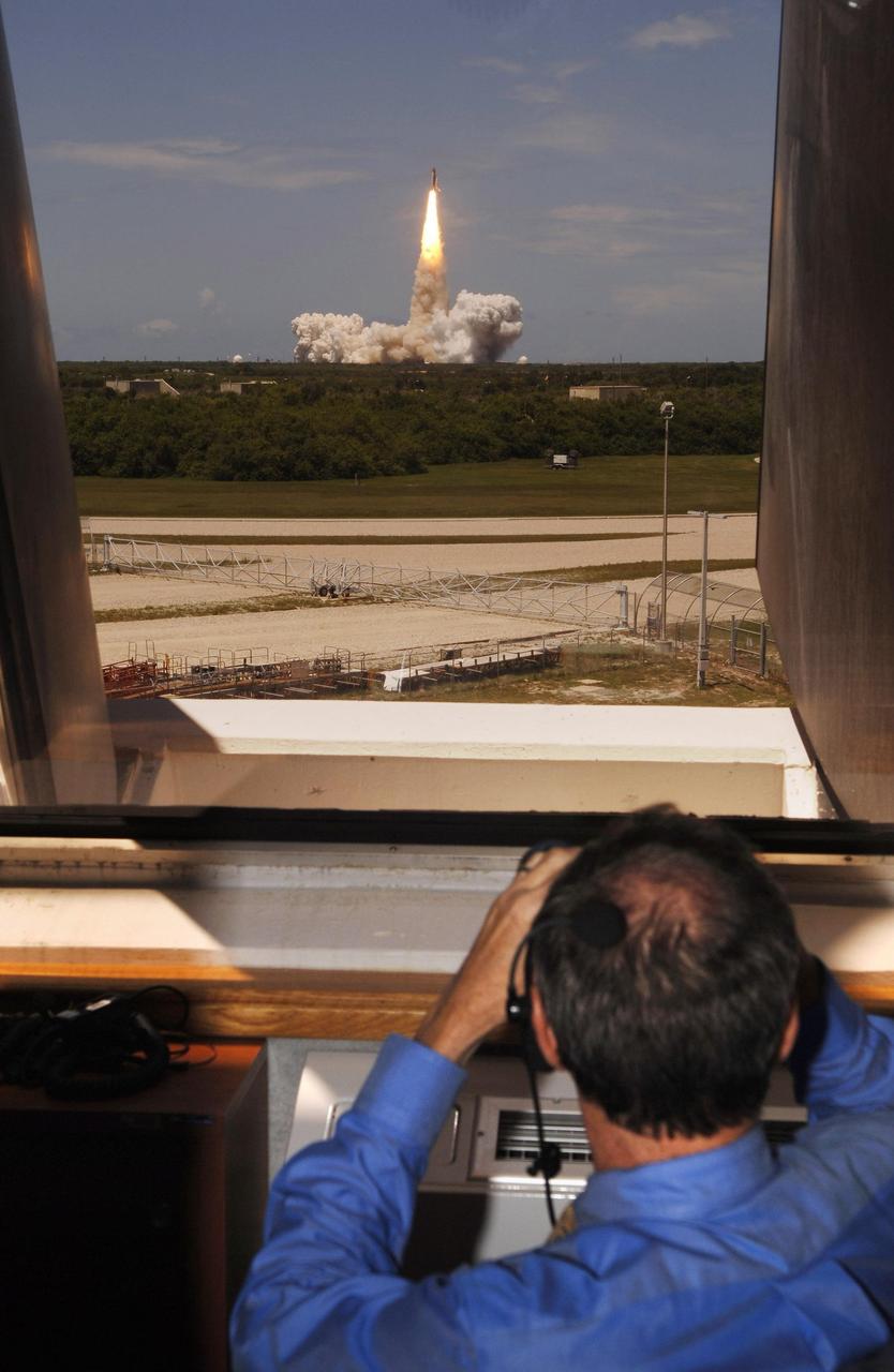 KENNEDY SPACE CENTER, FLA. -    From Firing Room 4 of the Launch Control Center, NASA Administrator Mike Griffin uses binoculars to view of the launch of Space Shuttle Discovery (in the background) on mission STS-121.  The launch made history as the first to occur on Independence Day.  Liftoff was on-time at 2:38 p.m. EDT.  During the 12-day mission, the STS-121 crew of seven will test new equipment and procedures to improve shuttle safety, as well as deliver supplies and make repairs to the International Space Station.  Landing is scheduled for July 16 or 17 at Kennedy's Shuttle Landing Facility.  Photo credit: NASA/Bill Ingalls