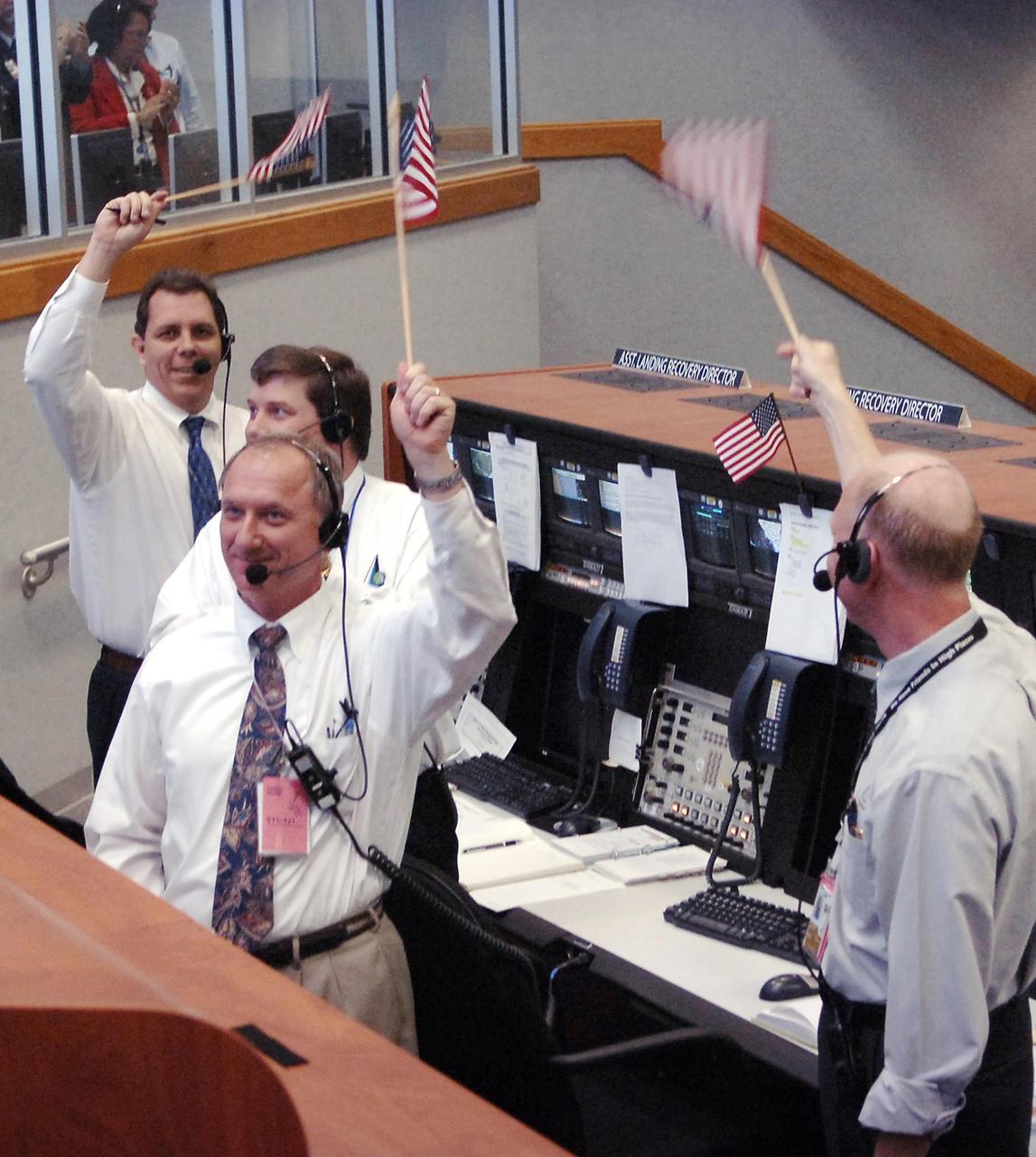 KENNEDY SPACE CENTER, FLA. -    In Firing Room 4 of the Launch Control Center, NASA launch team members cheer and wave American flags at the successful launch of Space Shuttle Discovery on mission STS-121.  The launch made history as the first to occur on Independence Day.  Liftoff was on-time at 2:38 p.m. EDT.  During the 12-day mission, the STS-121 crew of seven will test new equipment and procedures to improve shuttle safety, as well as deliver supplies and make repairs to the International Space Station.  Landing is scheduled for July 16 or 17 at Kennedy's Shuttle Landing Facility.  Photo credit: NASA/Bill Ingalls