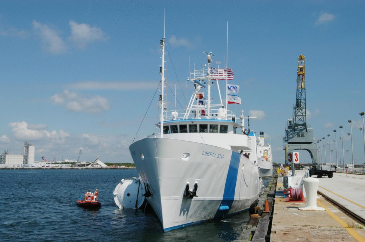 KENNEDY SPACE CENTER, FLA. - At a dock in Port Canaveral, the SRB Retrieval Ship Liberty Star transfers its tow cargo, a spent solid rocket booster, to a starboard position for the balance of its journey to Cape Canaveral Air Force Station. The booster is from Space Shuttle Discovery, which launched on July 4. The space shuttle’s solid rocket booster casings and associated flight hardware are recovered at sea. The boosters impact the Atlantic Ocean approximately seven minutes after liftoff. The splashdown area is a square of about 6 by 9 nautical miles located about 140 nautical miles downrange from the launch pad. The retrieval ships are stationed approximately 8 to 10 nautical miles from the impact area at the time of splashdown. As soon as the boosters enter the water, the ships accelerate to a speed of 15 knots and quickly close on the boosters. The pilot chutes and main parachutes are the first items to be brought on board. With the chutes and frustum recovered, attention turns to the boosters. The ship’s tow line is connected and the booster is returned to the Port and ,after transfer to a position alongside the ship, to Hangar AF at Cape Canaveral Air Force Station. There, the expended boosters are disassembled, refurbished and reloaded with solid propellant for reuse. Photo credit: NASA/George Shelton