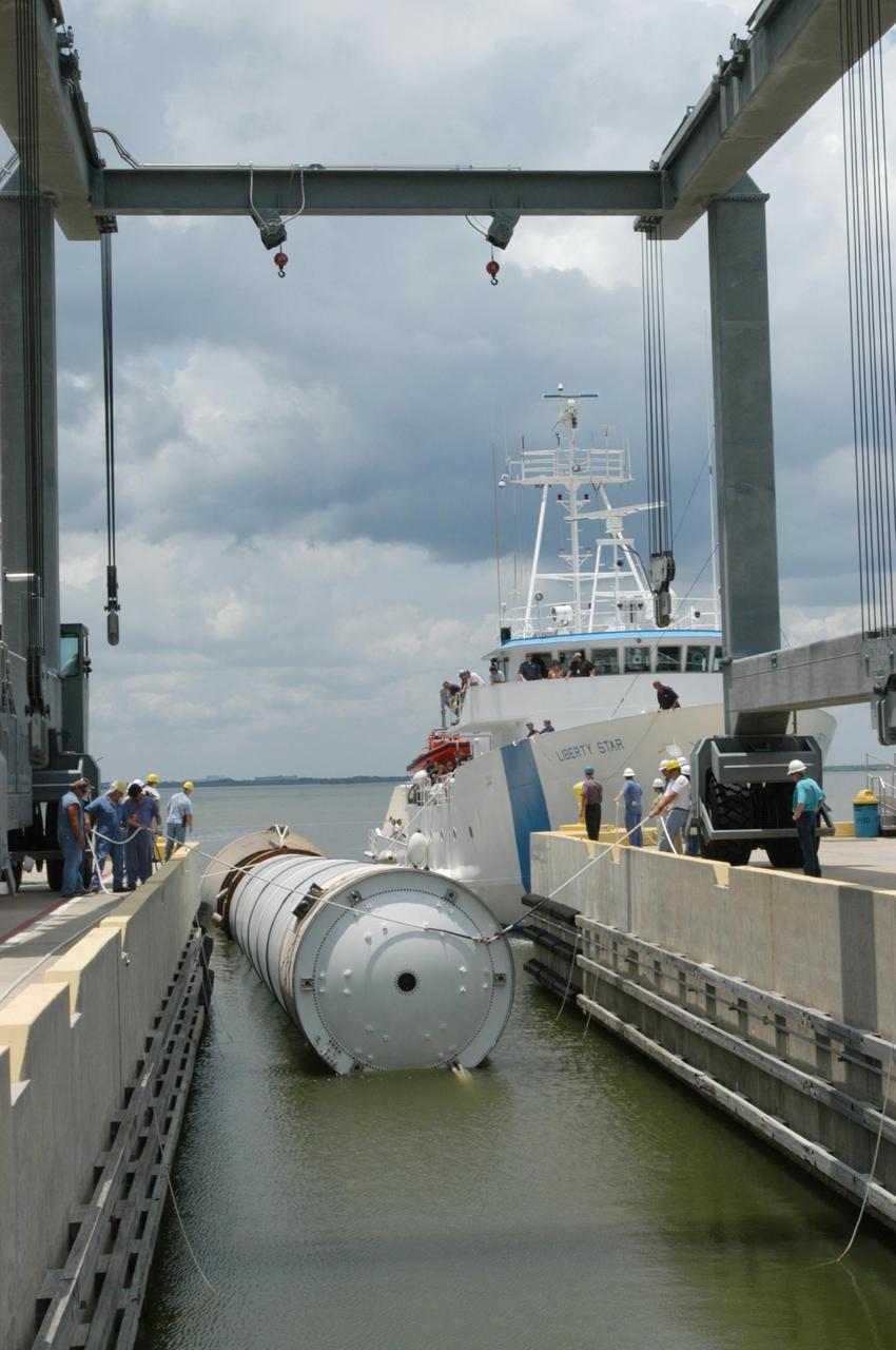 KENNEDY SPACE CENTER, FLA. -   At the dock at Hangar AF, Cape Canaveral Air Force Station, workers move the spent solid rocket booster away from the SRB Retrieval Ship Liberty Star to an area beneath the straddle crane that will lift it out of the water.  The booster is from Space Shuttle Discovery, which launched on July 4.  The space shuttle’s solid rocket booster casings and associated flight hardware are recovered at sea.  The boosters impact the Atlantic Ocean approximately seven minutes after liftoff. The splashdown area is a square of about 6 by 9 nautical miles located about 140 nautical miles downrange from the launch pad. The retrieval ships are stationed approximately 8 to 10 nautical miles from the impact area at the time of splashdown. As soon as the boosters enter the water, the ships accelerate to a speed of 15 knots and quickly close on the boosters.  The pilot chutes and main parachutes are the first items to be brought on board. With the chutes and frustum recovered, attention turns to the boosters. The ship’s tow line is connected and the booster is returned to the Port and ,after transfer to a position alongside the ship, to Hangar AF at Cape Canaveral Air Force Station.  There, the expended boosters are disassembled, refurbished and reloaded with solid propellant for reuse.  Photo credit: NASA/George Shelton