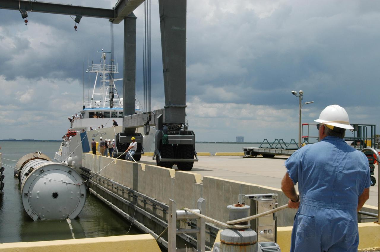 KENNEDY SPACE CENTER, FLA. -   At the dock at Hangar AF, Cape Canaveral Air Force Station, workers move the spent solid rocket booster underneath the straddle crane that will lift it out of the water.  The booster is from Space Shuttle Discovery, which launched on July 4. The space shuttle’s solid rocket booster casings and associated flight hardware are recovered at sea.  The boosters impact the Atlantic Ocean approximately seven minutes after liftoff. The splashdown area is a square of about 6 by 9 nautical miles located about 140 nautical miles downrange from the launch pad. The retrieval ships are stationed approximately 8 to 10 nautical miles from the impact area at the time of splashdown. As soon as the boosters enter the water, the ships accelerate to a speed of 15 knots and quickly close on the boosters.  The pilot chutes and main parachutes are the first items to be brought on board. With the chutes and frustum recovered, attention turns to the boosters. The ship’s tow line is connected and the booster is returned to the Port and ,after transfer to a position alongside the ship, to Hangar AF at Cape Canaveral Air Force Station.  There, the expended boosters are disassembled, refurbished and reloaded with solid propellant for reuse.  Photo credit: NASA/George Shelton