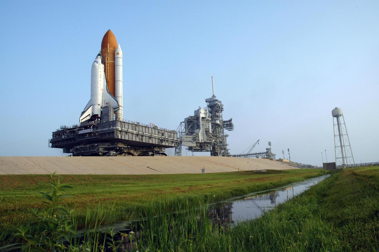 KENNEDY SPACE CENTER, FLA. - In the bright light of day, Space Shuttle Atlantis nears the hard stand on Launch Pad 39B. First motion out of the Vehicle Assembly Building was 1:05 a.m. The shuttle sits on top of the mobile launcher platform, which in turn rests on the crawler-transporter. At right is the 290-foot high, 300,000- gallon water tank that aids in sound suppression during launch. The water releases just prior to the ignition of the shuttle engines and flows through 7-foot-diameter pipes for about 20 seconds, pouring into 16 nozzles atop the flame deflectors and from outlets in the main engines exhaust hole in the mobile launcher platform. The slow speed of the crawler results in a 6-hour trek to the pad approximately 4 miles away. Atlantis' launch window begins Aug. 27 for an 11-day mission to the International Space Station. The STS-115 crew of six astronauts will continue construction of the station and install their cargo, the Port 3/4 truss segment with its two large solar arrays. Photo credit: NASA/Troy Cryder