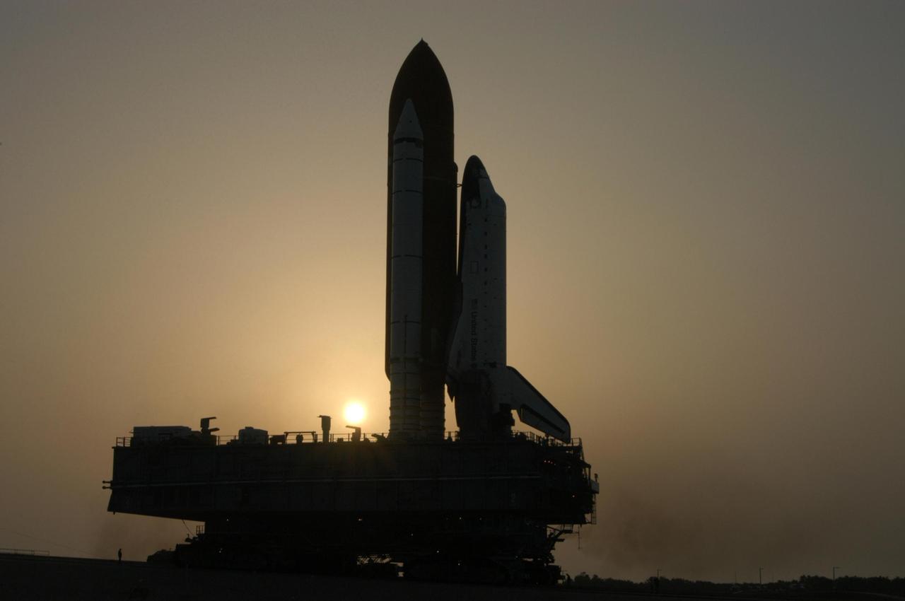 KENNEDY SPACE CENTER, FLA. - Silhouetted against the rising sun, Space Shuttle Atlantis rolls toward Launch Pad 39B. First motion out of the Vehicle Assembly Building was 1:05 a.m. The shuttle sits on top of the mobile launcher platform, which in turn rests on the crawler-transporter. The slow speed of the crawler results in a 6-hour trek to the pad approximately 4 miles away. Atlantis' launch window begins Aug. 27 for an 11-day mission to the International Space Station. The STS-115 crew of six astronauts will continue construction of the station and install their cargo, the Port 3/4 truss segment with its two large solar arrays. Photo credit: NASA/George Shelton