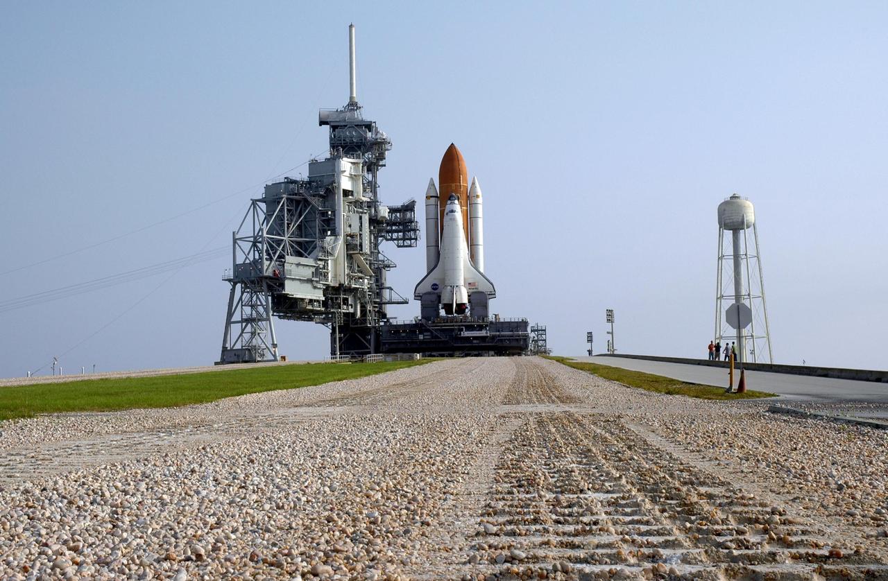 KENNEDY SPACE CENTER, FLA. - The tracks of the crawler-transporter are visible on the crawlerway (foreground) leading to Launch Pad 39B after the 4-mile journey of Space Shuttle Atlantis, which sits on the pad. At right is the 290-foot high, 300,000- gallon water tank that aids in sound suppression during launch. The water releases just prior to the ignition of the shuttle engines and flows through 7-foot-diameter pipes for about 20 seconds, pouring into 16 nozzles atop the flame deflectors and from outlets in the main engines exhaust hole in the mobile launcher platform. The slow speed of the crawler results in a 6-hour trek to the pad approximately 4 miles away. Atlantis' launch window begins Aug. 27 for an 11-day mission to the International Space Station. The STS-115 crew of six astronauts will continue construction of the station and install their cargo, the Port 3/4 truss segment with its two large solar arrays. Photo credit: NASA/Troy Cryder