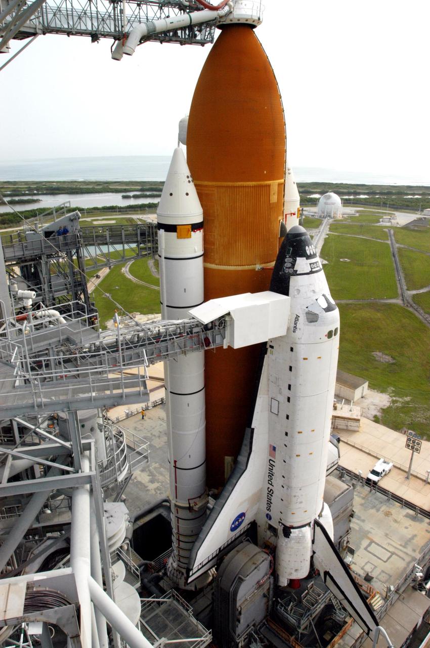 KENNEDY SPACE CENTER, FLA. - Space Shuttle Atlantis sits on the hardstand of Launch Pad 39B after its nearly 8-hour rollout from the Vehicle Assembly Building. The "beanie cap," at the end of the external tank gaseous oxygen vent arm, is extended over the top of the external tank. The cap is a vent hood that vacuums away the very cold liquid oxygen vapors as they boil off from the top of the external tank before launch. Lower down on the left is the orbiter access arm, with the White Room on the outer end, extended toward Atlantis' crew access hatch. Below the orbiter, on each side of the main engine nozzles, are the tail service masts that provide several umbilical connections to the orbiter, including a liquid-oxygen line through one and a liquid-hydrogen line through another. The slow speed of the crawler results in a 6- to 8-hour trek to the pad approximately 4 miles away. Atlantis' launch window begins Aug. 27 for an 11-day mission to the International Space Station. The STS-115 crew of six astronauts will continue construction of the station and install their cargo, the Port 3/4 truss segment with its two large solar arrays. Photo credit: NASA/Troy Cryder & George Shelton