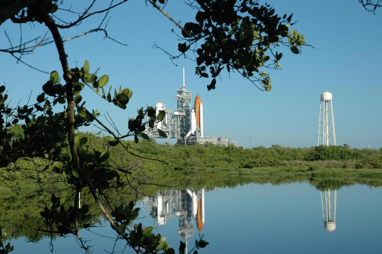 KENNEDY SPACE CENTER, FLA. - Viewed from across pond near Launch Pad 39B, Space Shuttle Atlantis is framed by tree limbs as it begins rolling back to the Vehicle Assembly Building. First motion off the pad was at 10:04 a.m. EDT. The rollback is a safety precaution as the area waits for the arrival of Tropical Storm Ernesto. The storm is forecast to be bringing 58-mph to 70-mph winds in the next 24 hours. The shuttle will be moved into high bay 2, on the southwest side of the VAB, for protection from the storm. Photo credit: NASA/Jack Pfaller