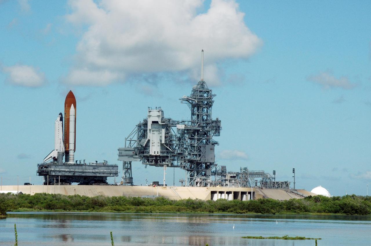 KENNEDY SPACE CENTER, FLA. - On Launch Pad 39B, the crawler-transporter moves Space Shuttle Atlantis away from the rotating and fixed service structures, at right, on its rollback to the Vehicle Assembly Building. First motion off the pad was at 10:04 a.m. EDT. The crawler is 131 feet long, 113 feet wide and 20 feet high. It weights 5.5 million pounds unloaded. The combined weight of crawler, mobile launcher platform and a space shuttle is 12 million pounds. Unloaded, the crawler moves at 2 mph. Loaded, the snail's pace slows to 1 mph. The rollback is a safety precaution as the area waits for the arrival of Tropical Storm Ernesto. The storm is forecast to be bringing 58-mph to 70-mph winds in the next 24 hours. The shuttle will be moved into high bay 2, on the southwest side of the VAB, for protection from the storm. Photo credit: NASA/Ken Thornsley