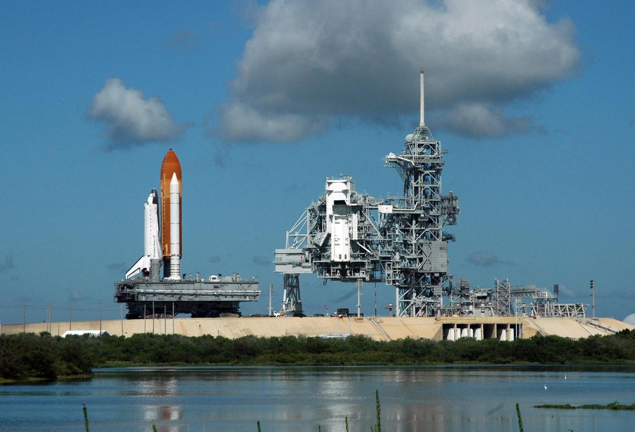 KENNEDY SPACE CENTER, FLA. - A darkening cloud overhead keeps vigil as Space Shuttle Atlantis moves away from Launch Pad 39B on its rollback to the Vehicle Assembly Building. At right are the rotating and fixed service structures. First motion off the pad was at 10:04 a.m. EDT. The crawler is 131 feet long, 113 feet wide and 20 feet high. It weights 5.5 million pounds unloaded. The combined weight of crawler, mobile launcher platform and a space shuttle is 12 million pounds. Unloaded, the crawler moves at 2 mph. Loaded, the snail's pace slows to 1 mph. The rollback is a safety precaution as the area waits for the arrival of Tropical Storm Ernesto. The storm is forecast to be bringing 58-mph to 70-mph winds in the next 24 hours. The shuttle will be moved into high bay 2, on the southwest side of the VAB, for protection from the storm. Photo credit: NASA/Ken Thornsley