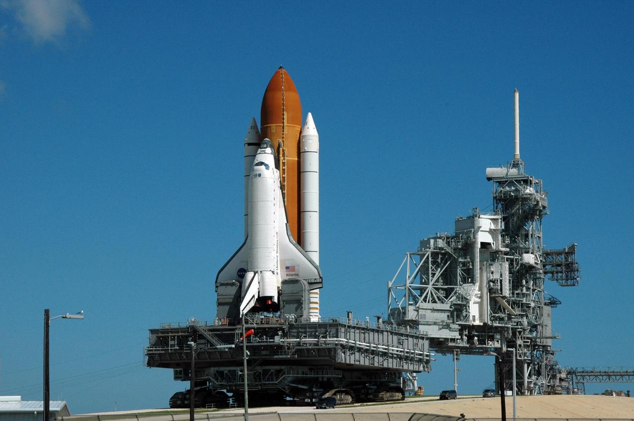 KENNEDY SPACE CENTER, FLA. - On Launch Pad 39B, the crawler-transporter moves Space Shuttle Atlantis along the ramp and away from the rotating and fixed service structures, at right, on its rollback to the Vehicle Assembly Building. First motion off the pad was at 10:04 a.m. EDT. The crawler is 131 feet long, 113 feet wide and 20 feet high. It weights 5.5 million pounds unloaded. The combined weight of crawler, mobile launcher platform and a space shuttle is 12 million pounds. Unloaded, the crawler moves at 2 mph. Loaded, the snail's pace slows to 1 mph. The rollback is a safety precaution as the area waits for the arrival of Tropical Storm Ernesto. The storm is forecast to be bringing 58-mph to 70-mph winds in the next 24 hours. The shuttle will be moved into high bay 2, on the southwest side of the VAB, for protection from the storm. Photo credit: NASA/Ken Thornsley