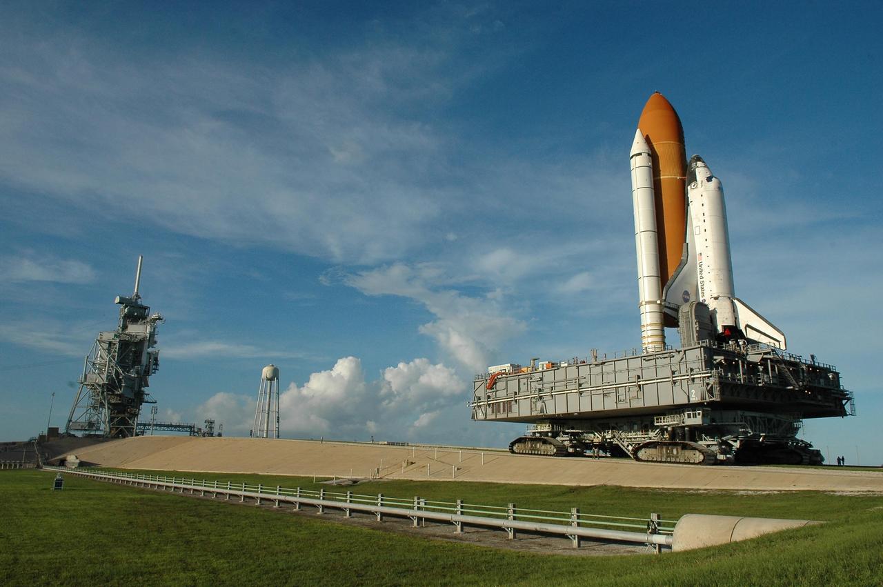 KENNEDY SPACE CENTER, FLA. - A late-day sun spotlights Space Shuttle Atlantis as it rolls up the ramp to Launch Pad 39B atop the crawler-transporter.   The crawler has a leveling system designed to keep the top of the space shuttle vertical while negotiating the 5-percent grade leading to the top of the launch pad. Also, a laser docking system provides almost pinpoint accuracy when the crawler and mobile launcher platform are positioned at the launch pad.  At left are the open rotating service structure and the fixed service structure topped by the 80-foot lightning mast. The shuttle had been moved off the launch pad due to concerns about the impact of Tropical Storm Ernesto, expected within 24 hours.  The forecast of lesser winds expected from Ernesto and its projected direction convinced Launch Integration Manager LeRoy Cain and Shuttle Launch Director Mike Leinbach to return the shuttle to the launch pad.   Photo credit: NASA/Kim Shiflett