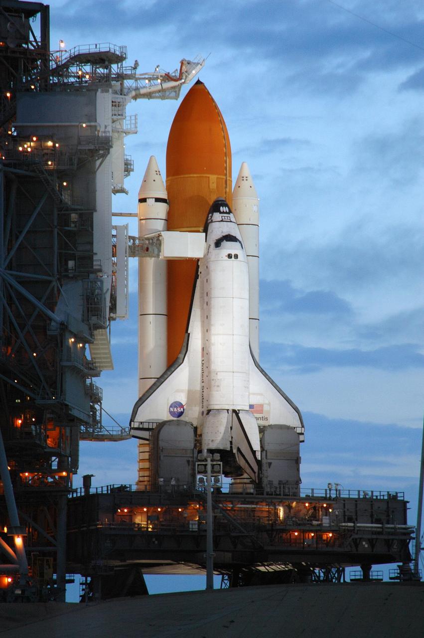 KENNEDY SPACE CENTER, FLA. -   The morning sky lightens behind Space Shuttle Atlantis while lights on the fixed service structure (FSS)  still illuminate the orbiter on Launch Pad 39B. Atlantis was originally scheduled to launch at 12:29 p.m. EDT on this date, but  a 24-hour scrub was called by mission managers due to a concern with Fuel Cell 1.  Seen poised above the orange external tank is the vent hood (known as the "beanie cap") at the end of the gaseous oxygen vent arm. Vapors are created as the liquid oxygen in the external tank boil off. The hood vents the gaseous oxygen vapors away from the space shuttle vehicle. Extending from the FSS to Atlantis is the orbiter access arm with the White Room at the end.  The White Room provides entry into the orbiter through the hatch.  During the STS-115 mission, Atlantis' astronauts will deliver and install the 17.5-ton, bus-sized P3/P4 integrated truss segment on the station. The girder-like truss includes a set of giant solar arrays, batteries and associated electronics and will provide one-fourth of the total power-generation capability for the completed station. This mission is the 116th space shuttle flight, the 27th flight for orbiter Atlantis, and the 19th U.S. flight to the International Space Station. STS-115 is scheduled to last 11 days with a planned landing at KSC.   Photo credit: NASA/Troy Cryder