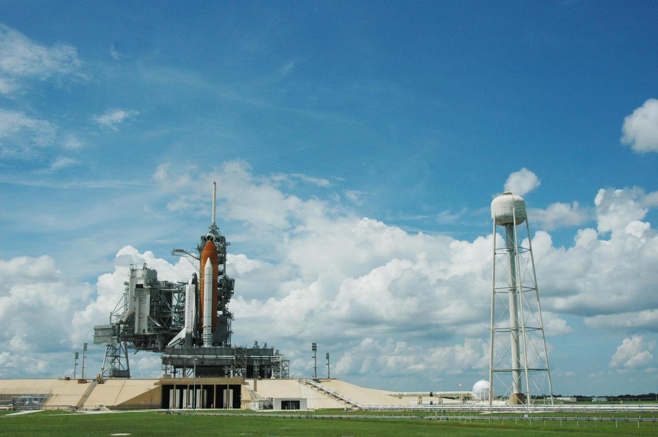 KENNEDY SPACE CENTER, FLA. -   Clouds spread throughout the sky behind Launch Pad 39B where Space Shuttle Atlantis still sits after the scrub of its launch on mission STS-115.  Atlantis was originally scheduled to launch at 12:29 p.m. EDT on this date, but  a 24-hour scrub was called by mission managers due to a concern with fuel cell 1.  Towering above the shuttle is the 80-foot lightning mast.  At right is the 300,000-gallon water tank that releases its contents onto the mobile launcher platform during liftoff to aid sound suppression.  During the STS-115 mission, Atlantis' astronauts will deliver and install the 17.5-ton, bus-sized P3/P4 integrated truss segment on the station. The girder-like truss includes a set of giant solar arrays, batteries and associated electronics and will provide one-fourth of the total power-generation capability for the completed station. This mission is the 116th space shuttle flight, the 27th flight for orbiter Atlantis, and the 19th U.S. flight to the International Space Station. STS-115 is scheduled to last 11 days with a planned landing at KSC.   Photo credit: NASA/Ken Thornsley