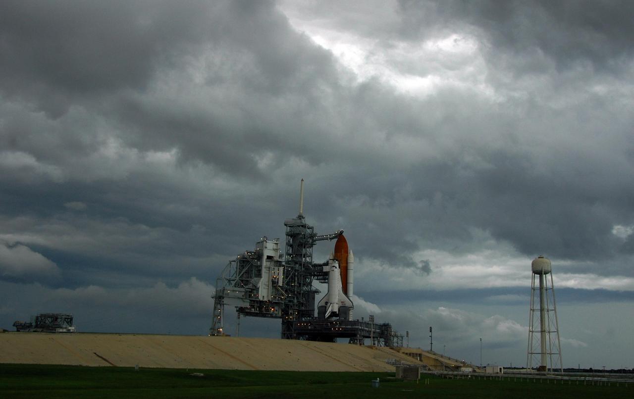 KENNEDY SPACE CENTER, FLA. -  Storm clouds fill the sky from Launch Pad 39B, at right, west beyond the Vehicle Assembly Building.  Space Shuttle Atlantis still sits on the pad after a scrub was called Aug. 27 due to a concern with fuel cell 1. Towering above the shuttle is the 80-foot lightning mast. During the STS-115 mission, Atlantis' astronauts will deliver and install the 17.5-ton, bus-sized P3/P4 integrated truss segment on the station. The girder-like truss includes a set of giant solar arrays, batteries and associated electronics and will provide one-fourth of the total power-generation capability for the completed station. This mission is the 116th space shuttle flight, the 27th flight for orbiter Atlantis, and the 19th U.S. flight to the International Space Station. STS-115 is scheduled to last 11 days with a planned landing at KSC.   Photo credit: NASA/Ken Thornsley