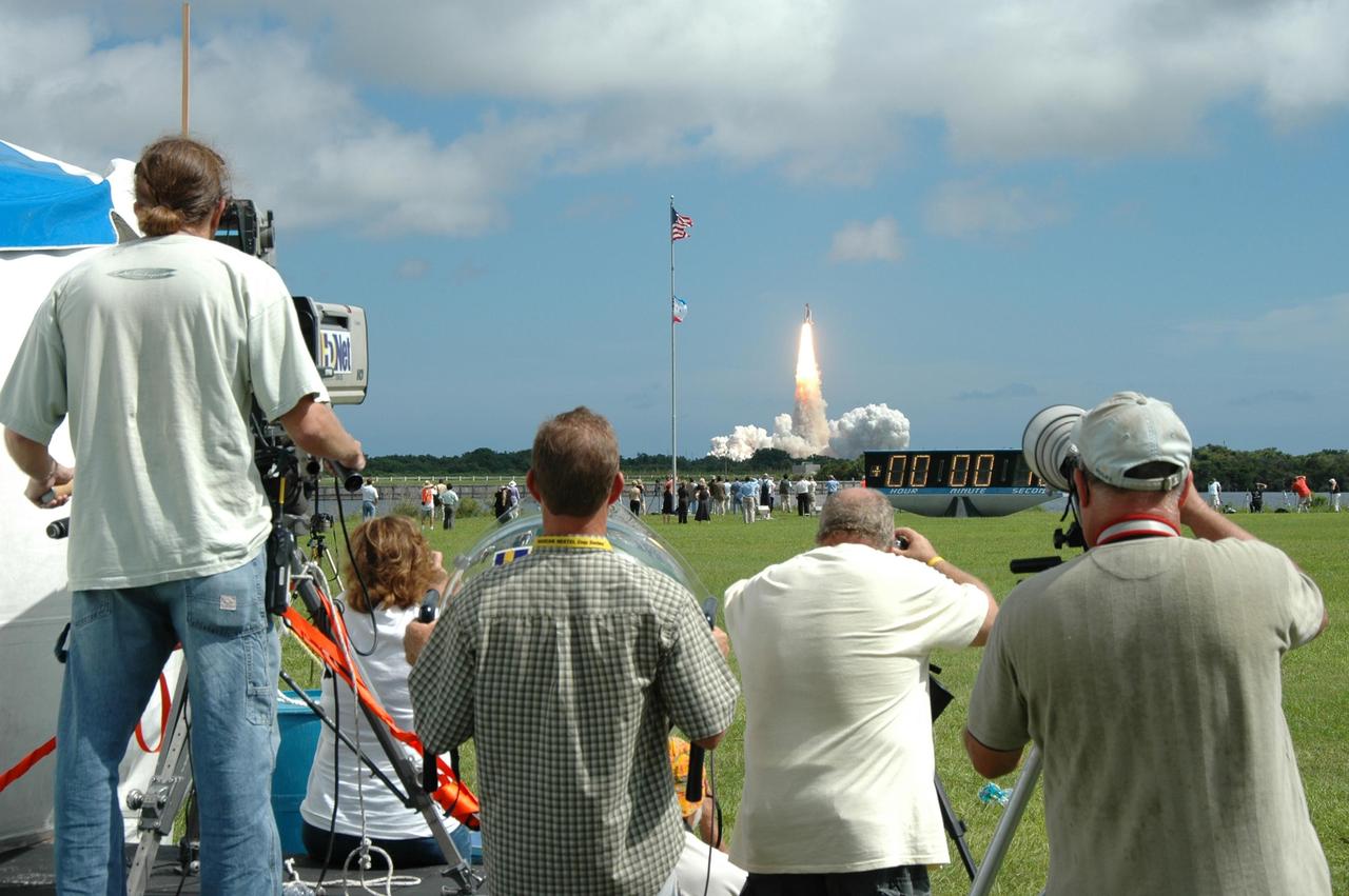 KENNEDY SPACE CENTER, FLA. - Space Shuttle Atlantis roars off the launch pad for a rendezvous with the International Space Station on mission STS-115.  In the foreground are only a few of the hundreds of photographers capturing the historic scene from the grounds of the NASA News Center.  Just beyond them is the countdown clock, marking launch and mission-elapsed time. After launch attempts were scrubbed Aug. 27 and 29 and Sept. 3 and 8 due to weather and technical concerns,  this launch was executed perfectly.  During the STS-115 mission, Atlantis' astronauts will deliver and install the 17.5-ton, bus-sized P3/P4 integrated truss segment on the station. The girder-like truss includes a set of giant solar arrays, batteries and associated electronics and will provide one-fourth of the total power-generation capability for the completed station. This mission is the 116th space shuttle flight, the 27th flight for orbiter Atlantis, and the 19th U.S. flight to the ISS. STS-115 is scheduled to last 11 days with a planned landing at KSC.  Photo credit: NASA/Jim Grossmann