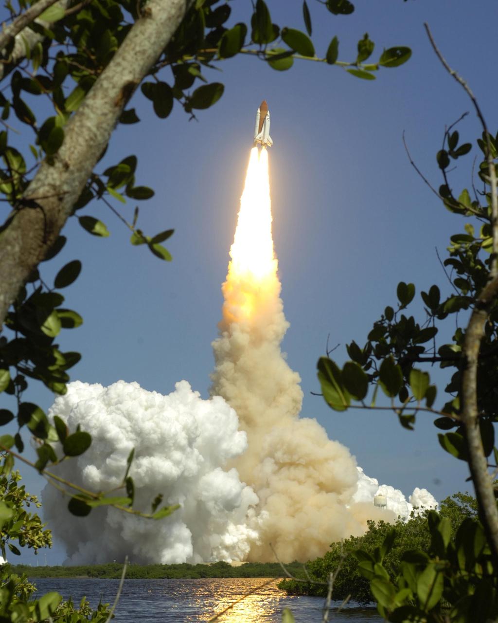 KENNEDY SPACE CENTER, FLA. -   Tree limbs frame the brilliant launch of Space Shuttle Atlantis as it flees the smoke and steam below, heading for a rendezvous with the International Space Station on mission STS-115.  Liftoff was on-time at 11:14:55 a.m. EDT.  After launch attempts were scrubbed Aug. 27 and 29 and Sept. 3 and 8 due to weather and technical concerns,  this launch was executed perfectly.  Mission STS-115 is the 116th space shuttle flight, the 27th flight for orbiter Atlantis, and the 19th U.S. flight to the International Space Station. During the mission, Atlantis' astronauts will deliver and install the 17.5-ton, bus-sized P3/P4 integrated truss segment on the station. The girder-like truss includes a set of giant solar arrays, batteries and associated electronics and will provide one-fourth of the total power-generation capability for the completed station. STS-115 is scheduled to last 11 days with a planned landing at KSC. Photo courtesy of Nikon/Scott Andrews