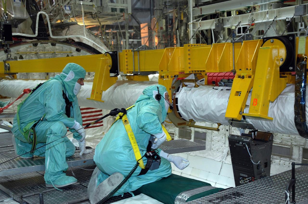 KENNEDY SPACE CENTER, FLA. -  In the Orbiter Processing Facility’s bay 1, workers watch closely as the orbiter boom sensor system is lowered into place on the starboard side of Atlantis’s payload bay for mission STS-117. The 50-foot-long boom attaches to the shuttle arm and provides equipment to inspect the shuttle's heat shield while in space.  It contains an intensified television camera (ITVC) and a laser dynamic range imager, which are mounted on a pan and tilt unit, and a laser camera system (LCS) mounted on a stationary bracket. Mission STS-117 will carry the S3/S4 arrays for installation on the International Space Station.  Launch of Space Shuttle Atlantis is scheduled for March.  Photo credit: NASA/Jack Pfaller