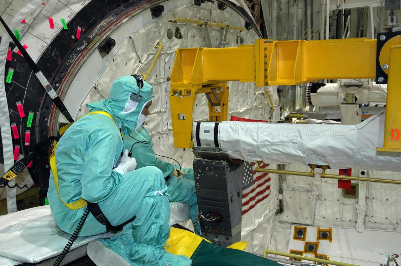 KENNEDY SPACE CENTER, FLA. -   In the Orbiter Processing Facility’s bay 1, workers watch closely as the orbiter boom sensor system is lowered into place on the starboard side of Atlantis’s payload bay for mission STS-117.  The 50-foot-long boom attaches to the shuttle arm and provides equipment to inspect the shuttle's heat shield while in space.  It contains an intensified television camera (ITVC) and a laser dynamic range imager, which are mounted on a pan and tilt unit, and a laser camera system (LCS) mounted on a stationary bracket. Mission STS-117 will carry the S3/S4 arrays for installation on the International Space Station.  Launch of Space Shuttle Atlantis is scheduled for March.  Photo credit: NASA/Jack Pfaller