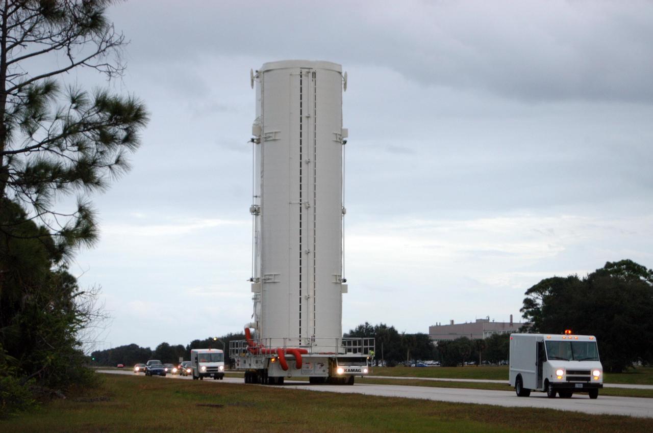 KENNEDY SPACE CENTER, FLA. --  The payload canister transporter carries its cargo very slowly along the road to Launch Pad 39B for mission STS-116.  Inside the canister are the SPACEHAB module and the port 5 truss segment, which will be moved into the payload changeout room at the pad and transferred into Space Shuttle Discovery's payload bay once the vehicle has rolled out to the pad. The payload canister is 65 feet long, 18 feet wide and 18 feet, 7 inches high. It has the capability to carry vertically or horizontally processed payloads up to 15 feet in diameter and 60 feet long, matching the capacity of the orbiter payload bay. It can carry payloads weighing up to 65,000 pounds. Clamshell-shaped doors at the top of the canister operate like the orbiter payload bay doors, with the same allowable clearances. Photo credit: NASA/George Shelton