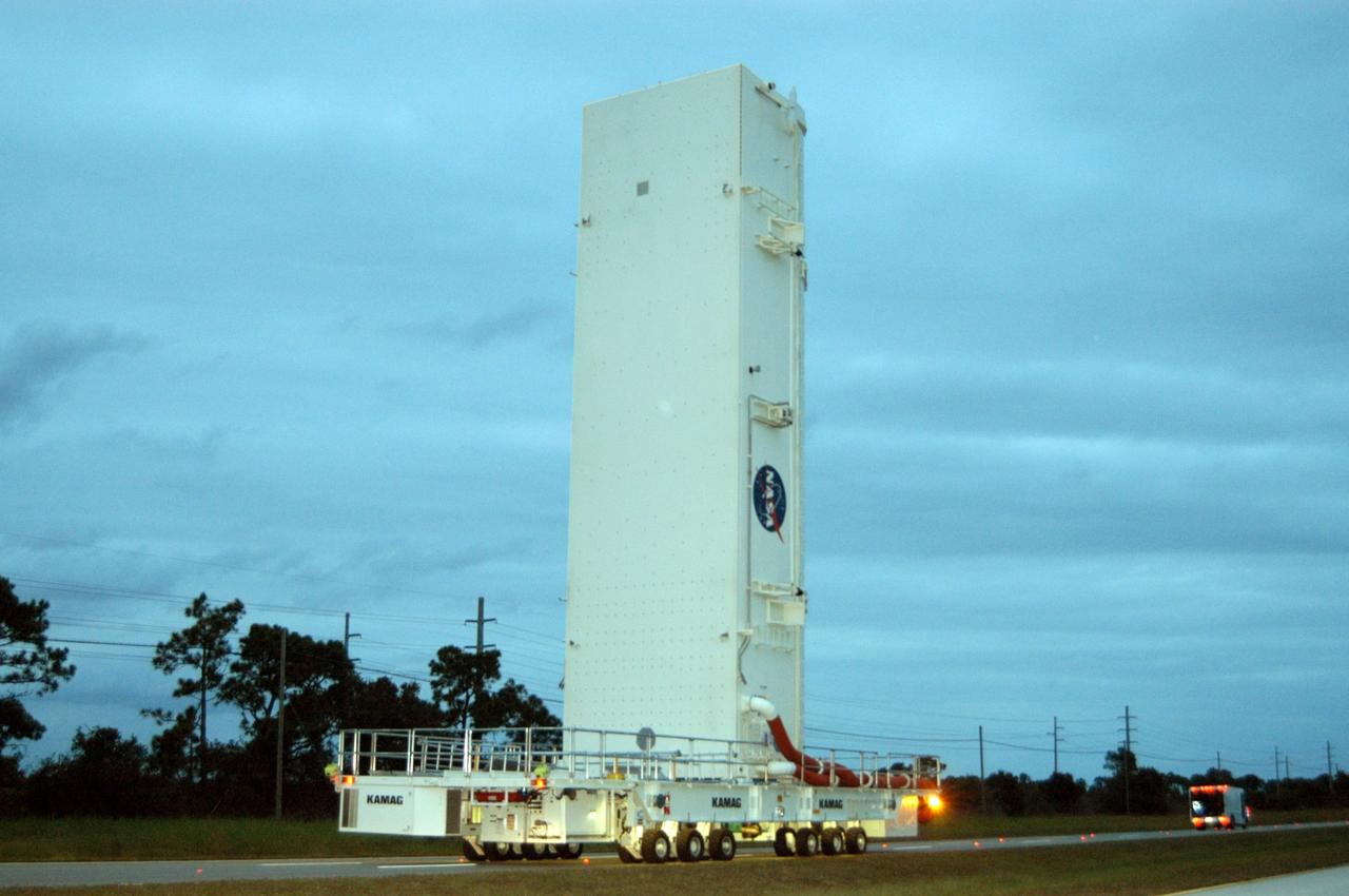 KENNEDY SPACE CENTER, FLA. --   Under a darkening, cloud-covered sky, the payload canister transporter carries its cargo very slowly along the road to Launch Pad 39B for mission STS-116.  Inside the canister are the SPACEHAB module and the port 5 truss segment, which will be moved into the payload changeout room at the pad and transferred into Space Shuttle Discovery's payload bay once the vehicle has rolled out to the pad. The payload canister is 65 feet long, 18 feet wide and 18 feet, 7 inches high. It has the capability to carry vertically or horizontally processed payloads up to 15 feet in diameter and 60 feet long, matching the capacity of the orbiter payload bay. It can carry payloads weighing up to 65,000 pounds. Clamshell-shaped doors at the top of the canister operate like the orbiter payload bay doors, with the same allowable clearances. Photo credit: NASA/George Shelton