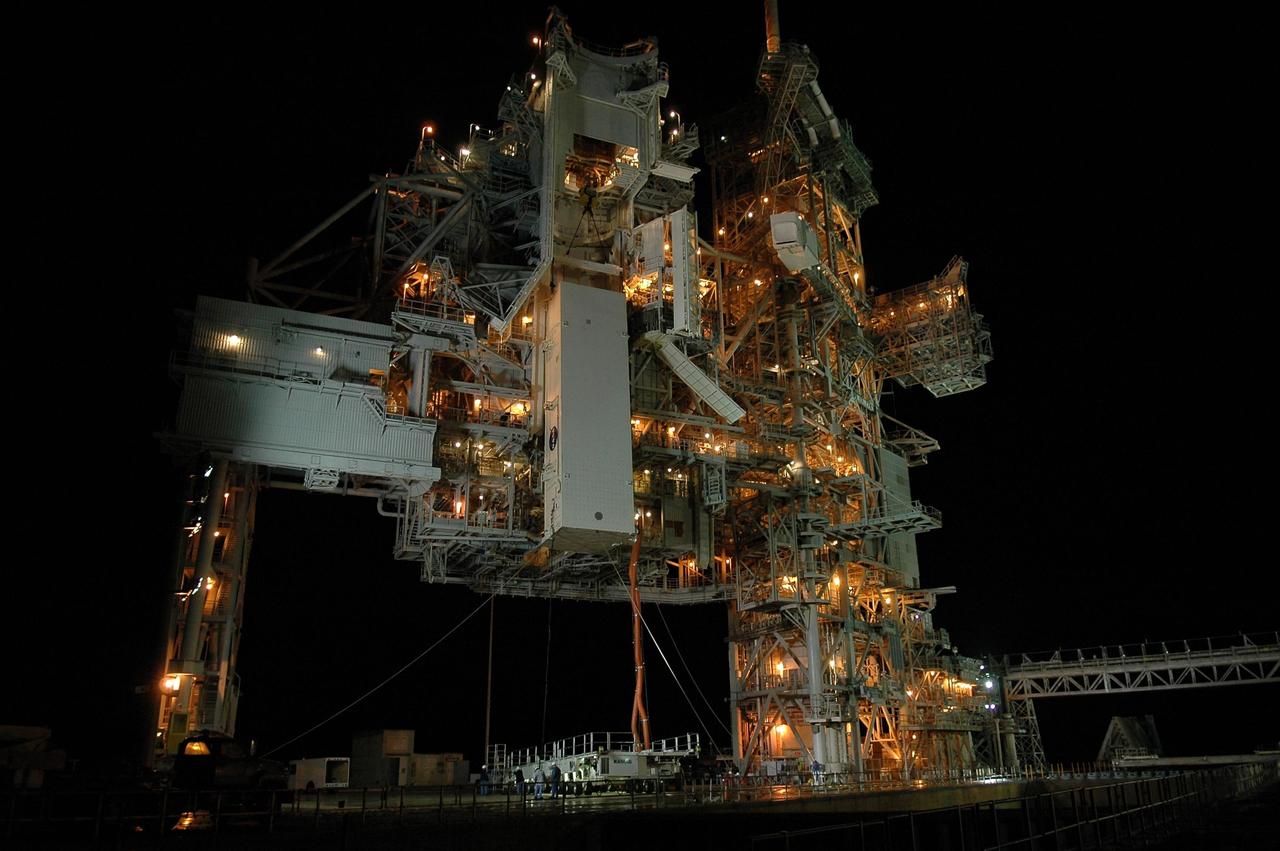 KENNEDY SPACE CENTER, FLA. --  With umbilical lines still attached, the payload canister is lifted up to the payload changeout room (PCR) on the rotating service structure (RSS) on Launch Pad 39B.  Inside the canister are the SPACEHAB module and the port 5 truss segment for mission STS-116.  Once inside the PCR, they will be transferred into Space Shuttle Discovery's payload bay after the vehicle has rolled out to the pad.  On the right is the fixed service structure.  The PCR is the enclosed, environmentally controlled portion of the RSS that supports cargo delivery to the pad and subsequent vertical installation into the orbiter payload bay. Seals around the mating surface of the PCR fit against the orbiter and allow the opening of the payload bay or canister doors and removal of the cargo without exposure to outside air and contaminants. A clean-air purge in the PCR maintains environmental control during PCR cargo operations. Cargo is removed from the payload canister and installed vertically in the orbiter by the payload ground handling mechanism (PGHM). Photo credit: NASA/Kim Shiflett