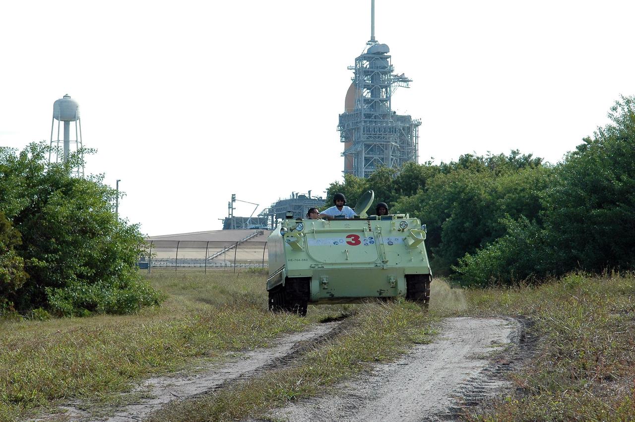 KENNEDY SPACE CENTER, FLA. --   STS-116 Mission Specialist Joan Higginbotham practices driving the M-113 armored personnel carrier away from Launch Pad 39B. On the M-113, Pilot William Oefelein is at left and Capt. George Hoggard, who is astronaut rescue team leader, in between Oefelein and Higginbotham. In the background is the fixed service structure, with the 80-foot-tall lightning mast on top, and Space Shuttle Discovery -- only the orange external tank can be seen. The mission crew is at KSC for terminal countdown demonstration test (TCDT) activities that are preparation for launch. The M-113 could be used to move the crew quickly away from the launch pad in the event of an emergency. The STS-116 mission is No. 20 to the International Space Station and construction flight 12A.1.  The mission payload is the SPACEHAB module, the P5 integrated truss structure and other key components. Launch is scheduled for no earlier than Dec. 7.  Photo credit: NASA/Kim Shiflett