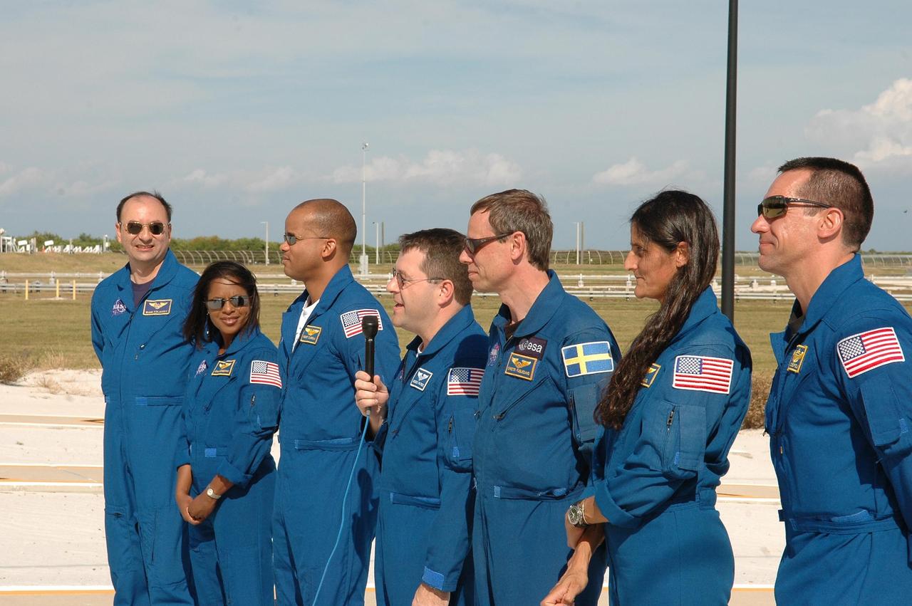 KENNEDY SPACE CENTER, FLA. -- The STS-116 crew pause in their prelaunch activities to talk to the media (foreground) at Launch Pad 39B. Mission Specialist Nicholas Patrick has the microphone to answer a question. From left, the crew members are Commander Mark Polansky, Mission Specialists Joan Higginbotham, Robert Curbeam, Patrick, Christer Fuglesang and Sunita Williams, and Pilot William Oefelein. Fuglesang represents the European Space Agency. The mission crew is at KSC for the TCDT, which includes a simulated launch countdown. The STS-116 mission is No. 20 to the International Space Station and construction flight 12A.1. The mission payload is the SPACEHAB module, the P5 integrated truss structure and other key components. Launch is scheduled for no earlier than Dec. 7. Photo credit: NASA/Kim Shiflett