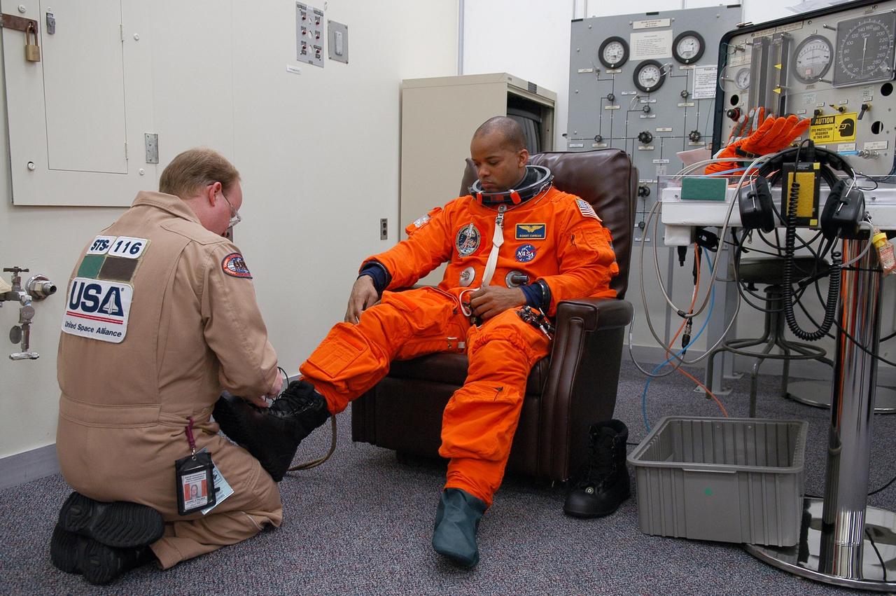 KENNEDY SPACE CENTER, FLA. --  The STS-116 mission crew practices for launch with a simulation of activities, from crew breakfast and suit-up to countdown in the orbiter.  In this photo Mission Specialist Robert Curbeam gets help fitting his boot before heading to Launch Pad 39B.  The STS-116 mission is No. 20 to the International Space Station and construction flight 12A.1.  The mission payload is the SPACEHAB module, the P5 integrated truss structure and other key components. Launch is scheduled for no earlier than Dec. 7. Photo credit: NASA/Kim Shiflett
