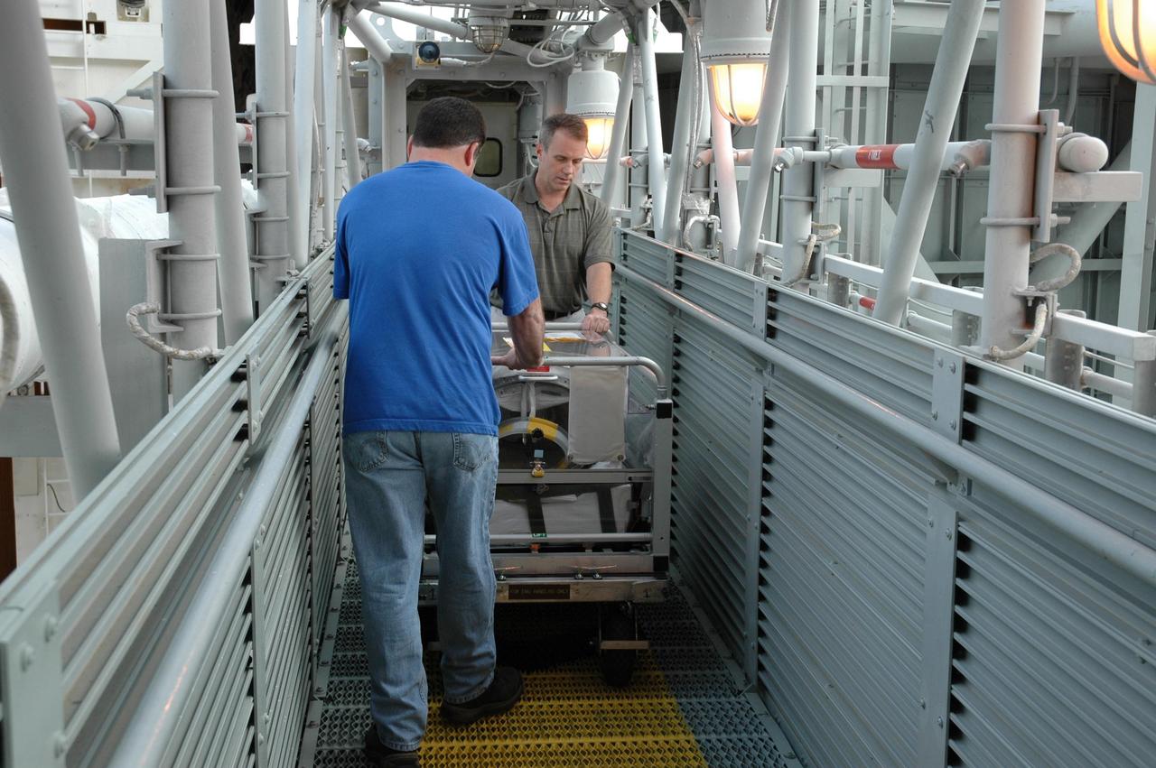 KENNEDY SPACE CENTER, FLA. --  Two workers on Launch Pad 39B maneuver a cart along the orbiter access arm toward the White Room.  The cart contains the extravehicular mobility units (or spacewalk suits) to be used on mission STS-116.  The suits will be stored inside Space Shuttle Discovery, which has access from the White Room.  Launch of Discovery is scheduled for 9:35 p.m. Dec. 7. The crew will deliver the P5 integrated truss to the International Space Station and install it during one or more extravehicular activities. Photo credit: NASA/Jack Pfaller