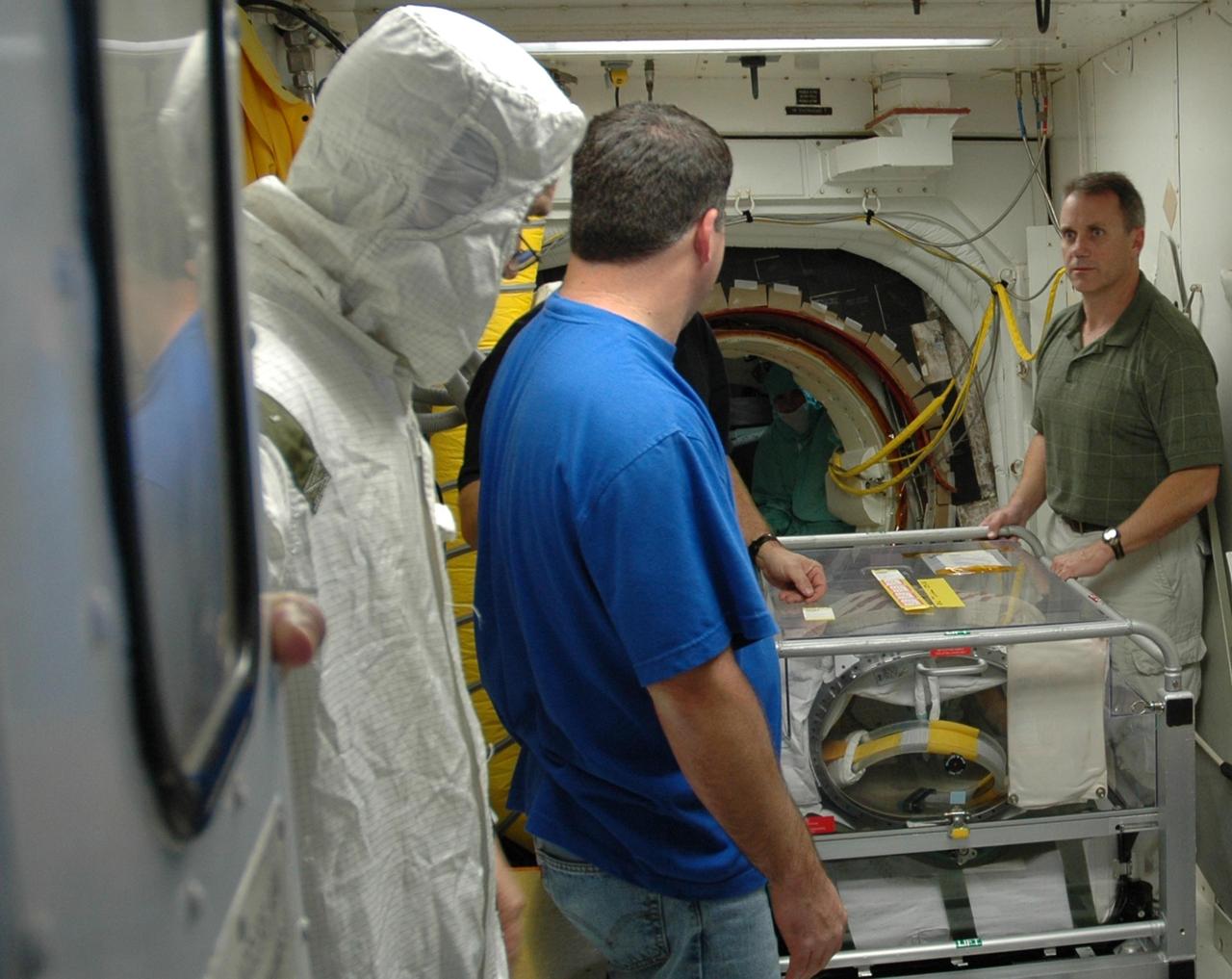 KENNEDY SPACE CENTER, FLA. --  Inside the White Room on Launch Pad 39B, workers get ready to move a cart through the hatch into Space Shuttle Discovery.  The cart contains the extravehicular mobility units (or spacewalk suits) to be used on mission STS-116.  The suits will be stored inside Discovery.  Launch of Discovery is scheduled for 9:35 p.m. Dec. 7. The crew will deliver the P5 integrated truss to the International Space Station and install it during one or more extravehicular activities. Photo credit: NASA/Jack Pfaller