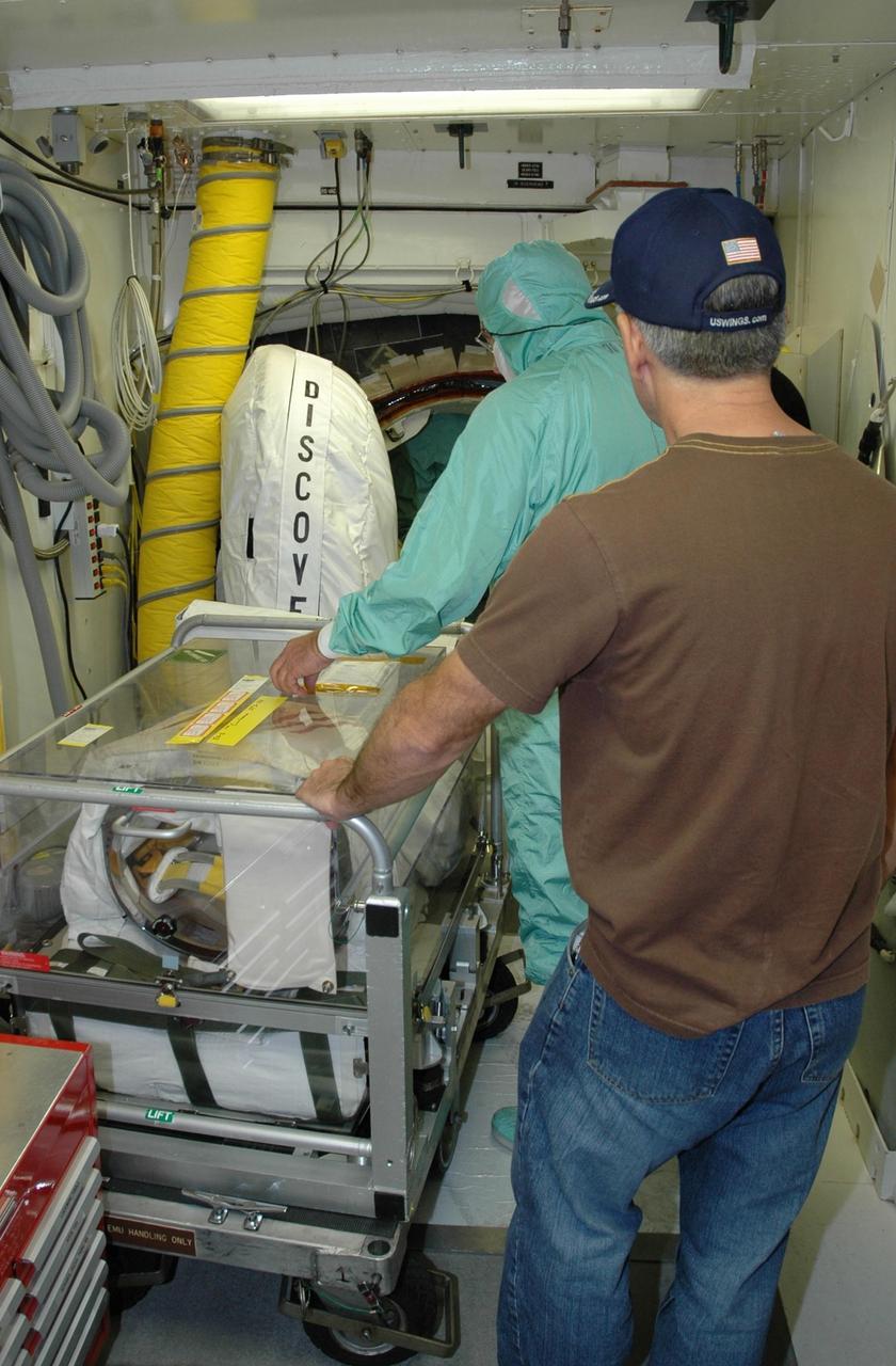 KENNEDY SPACE CENTER, FLA. --  Inside the White Room on Launch Pad 39B, the worker in the foreground hands off the cart to another worker in a protective suit who will move it inside Space Shuttle Discovery for storage. The cart contains the extravehicular mobility units (or spacewalk suits) to be used on mission STS-116.  Launch of Discovery is scheduled for 9:35 p.m. Dec. 7. The crew will deliver the P5 integrated truss to the International Space Station and install it during one or more extravehicular activities. Photo credit: NASA/Jack Pfaller